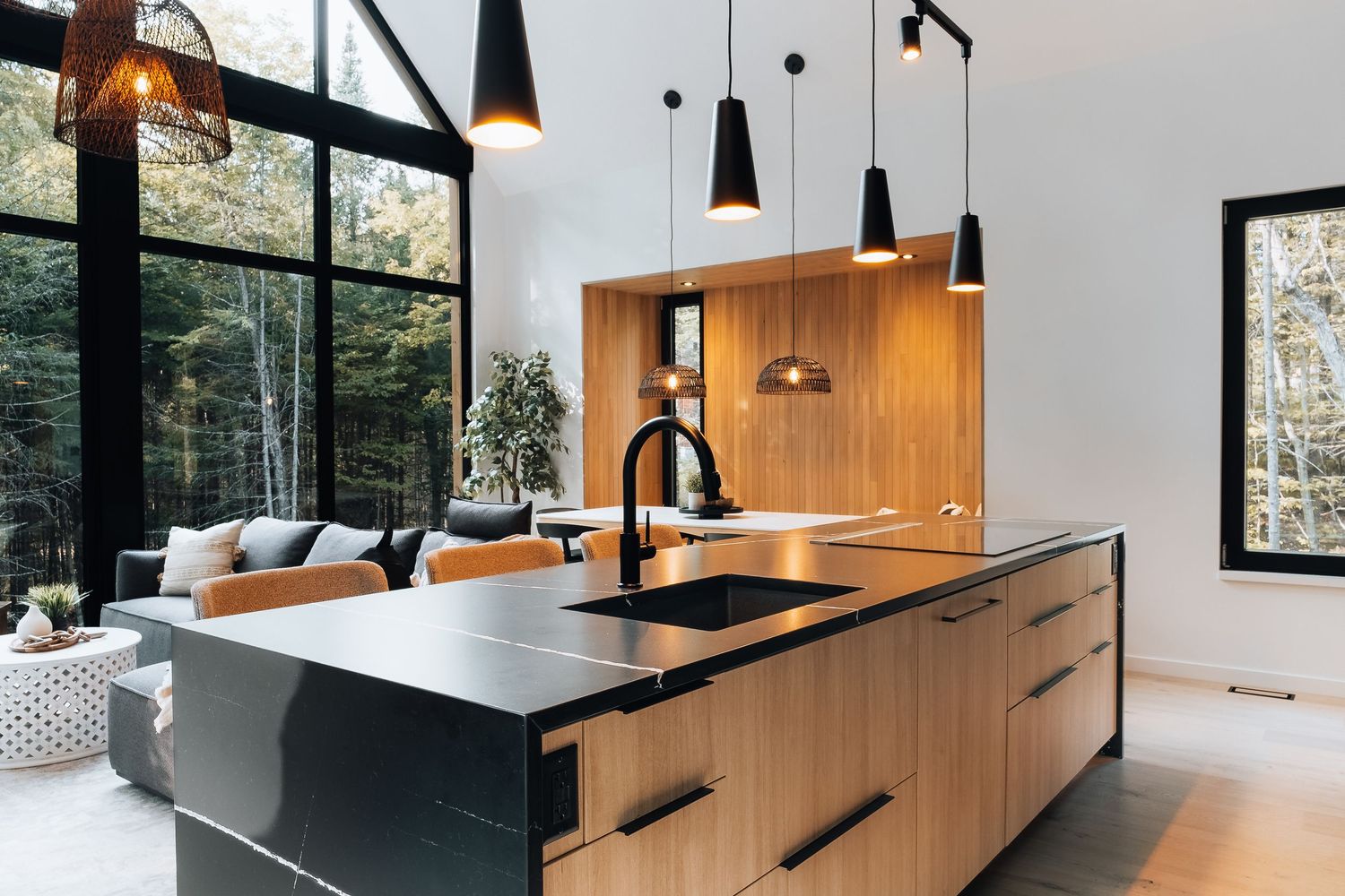 Spacious kitchen island with black countertop and wooden cabinetry featuring pendant lighting and forest views.