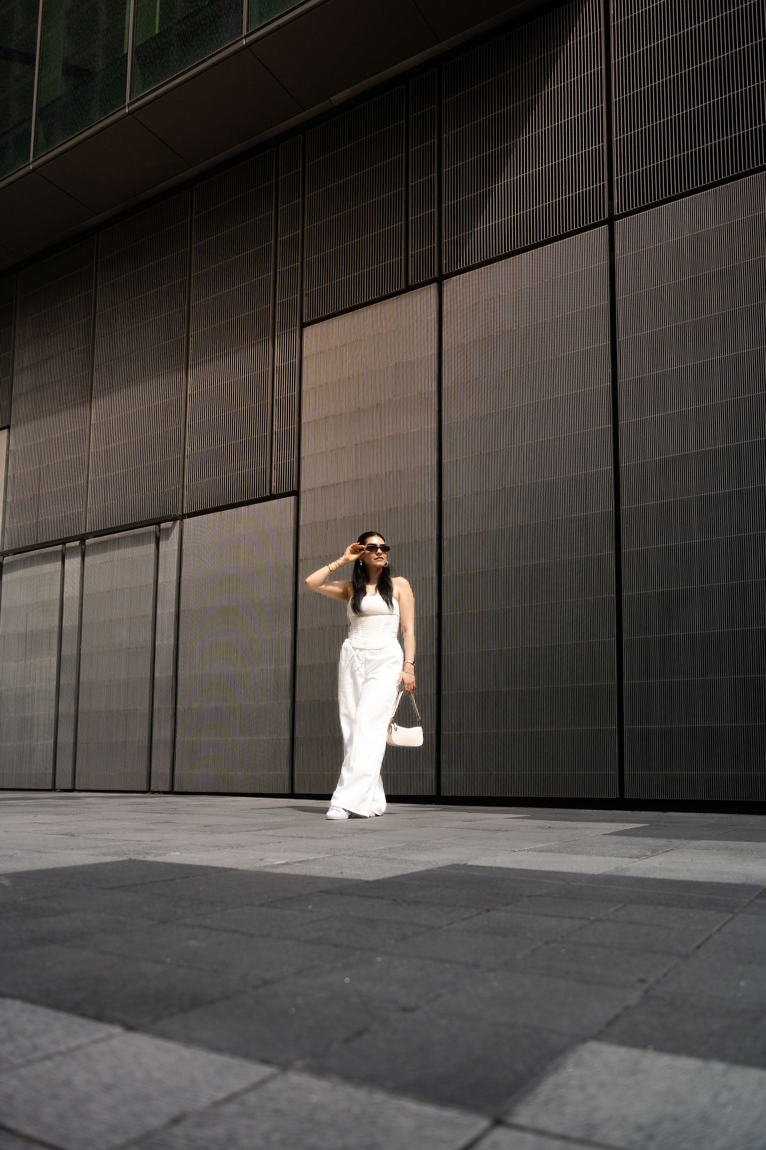 Person in white outfit walks along modern building with dark geometric walls.
