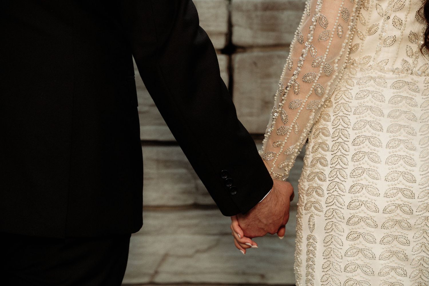 Elegant lace wedding dress details shown as couple holds hands during ceremony.