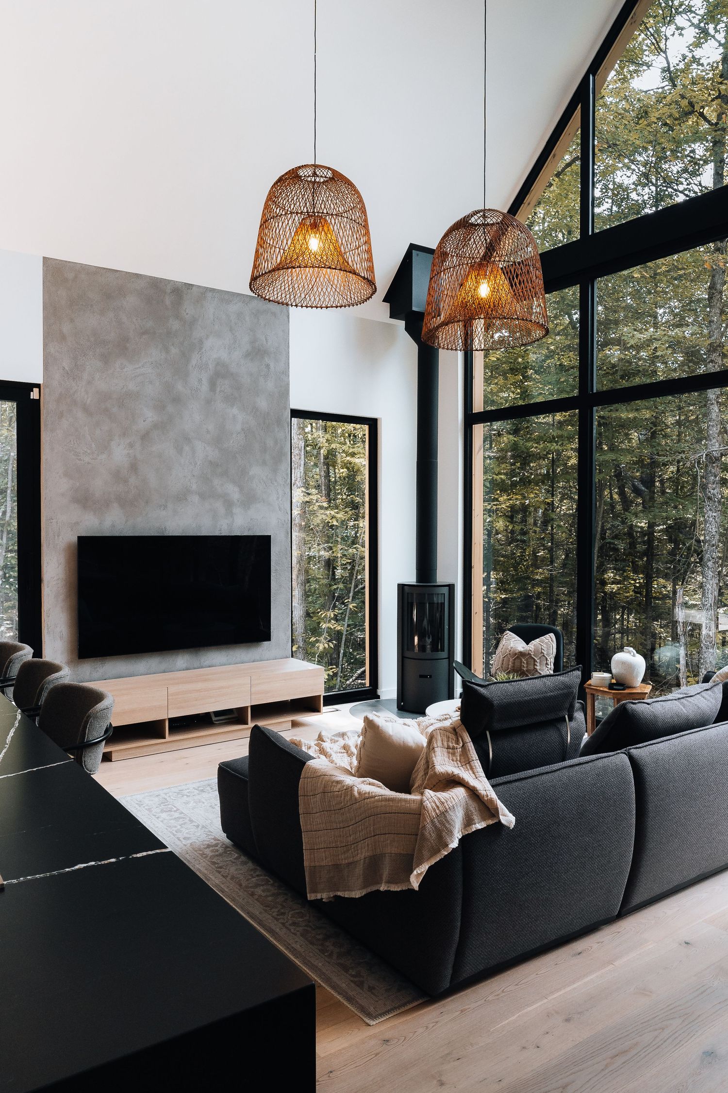 Modern living room with black sofa, large windows, and forest views showcasing contemporary minimalist design.