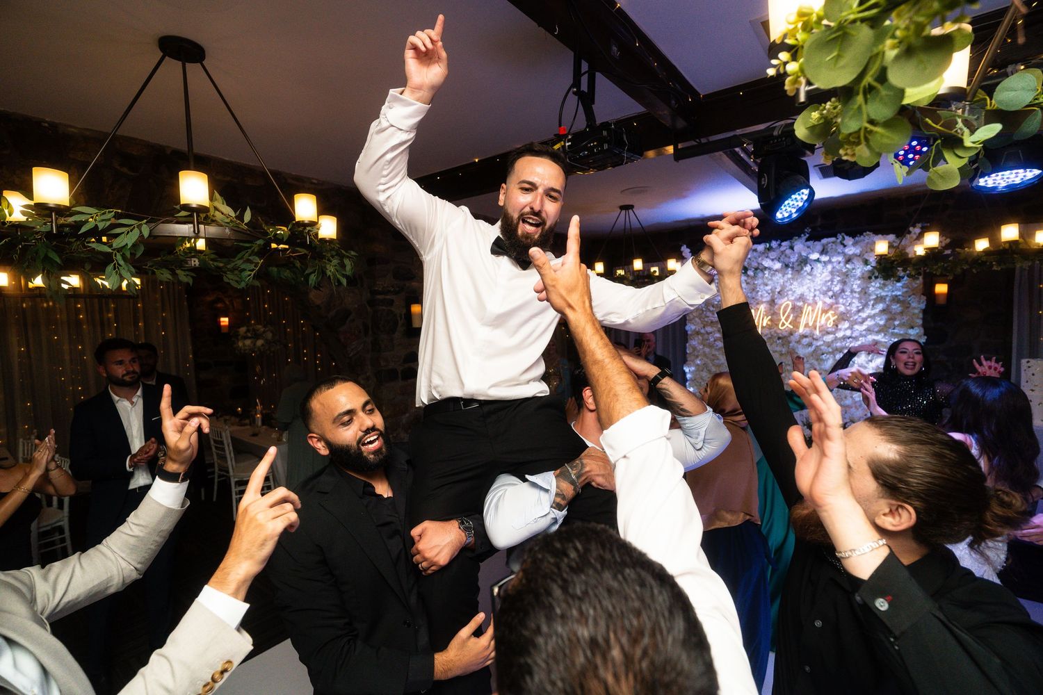 A group of people dancing and celebrating at a dimly lit nightclub or party venue with string lights overhead.
