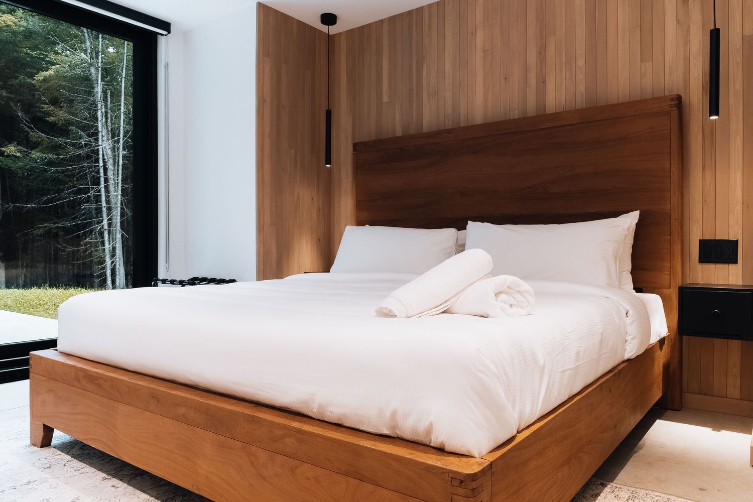 Contemporary bedroom with wooden wall panels and large windows overlooking natural scenery.