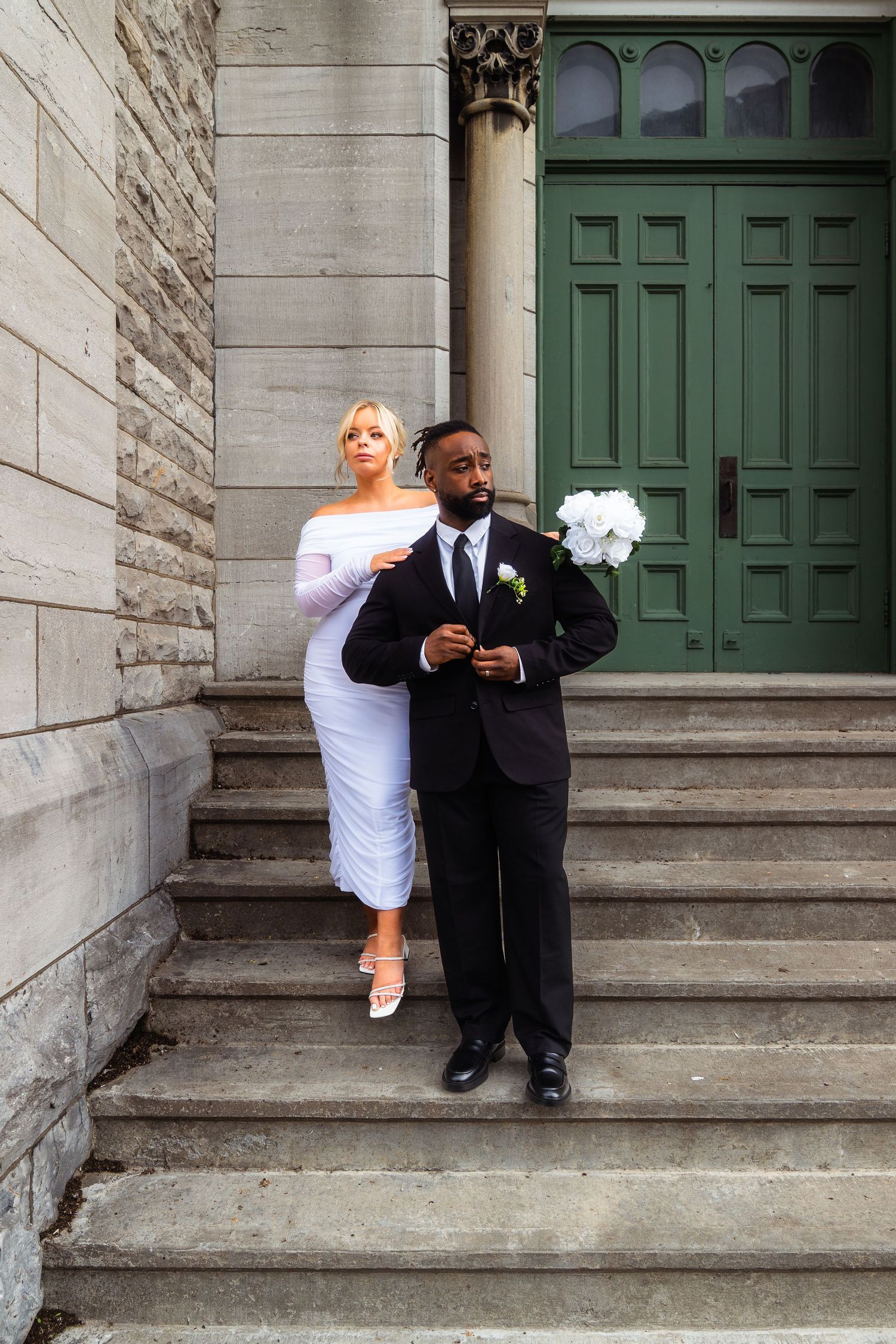 A couple in black and white attire sit casually on stone steps of a historic building.