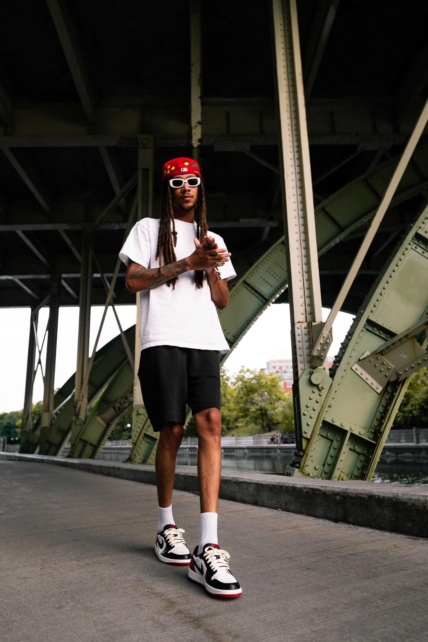 Low angle shot of person wearing white shirt and sneakers walking under bridge structure.