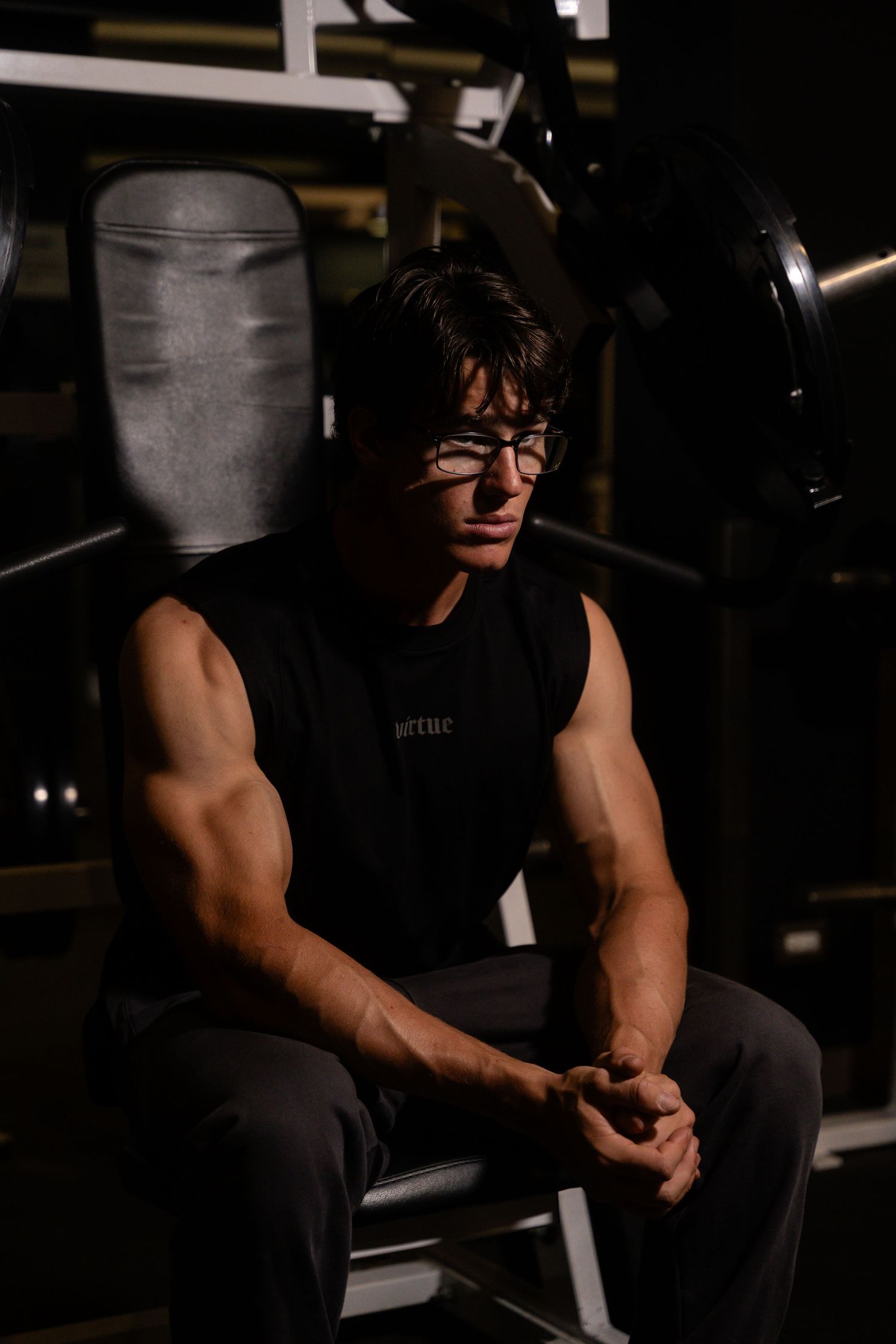 Side view of person sitting on gym equipment in dark atmospheric lighting.