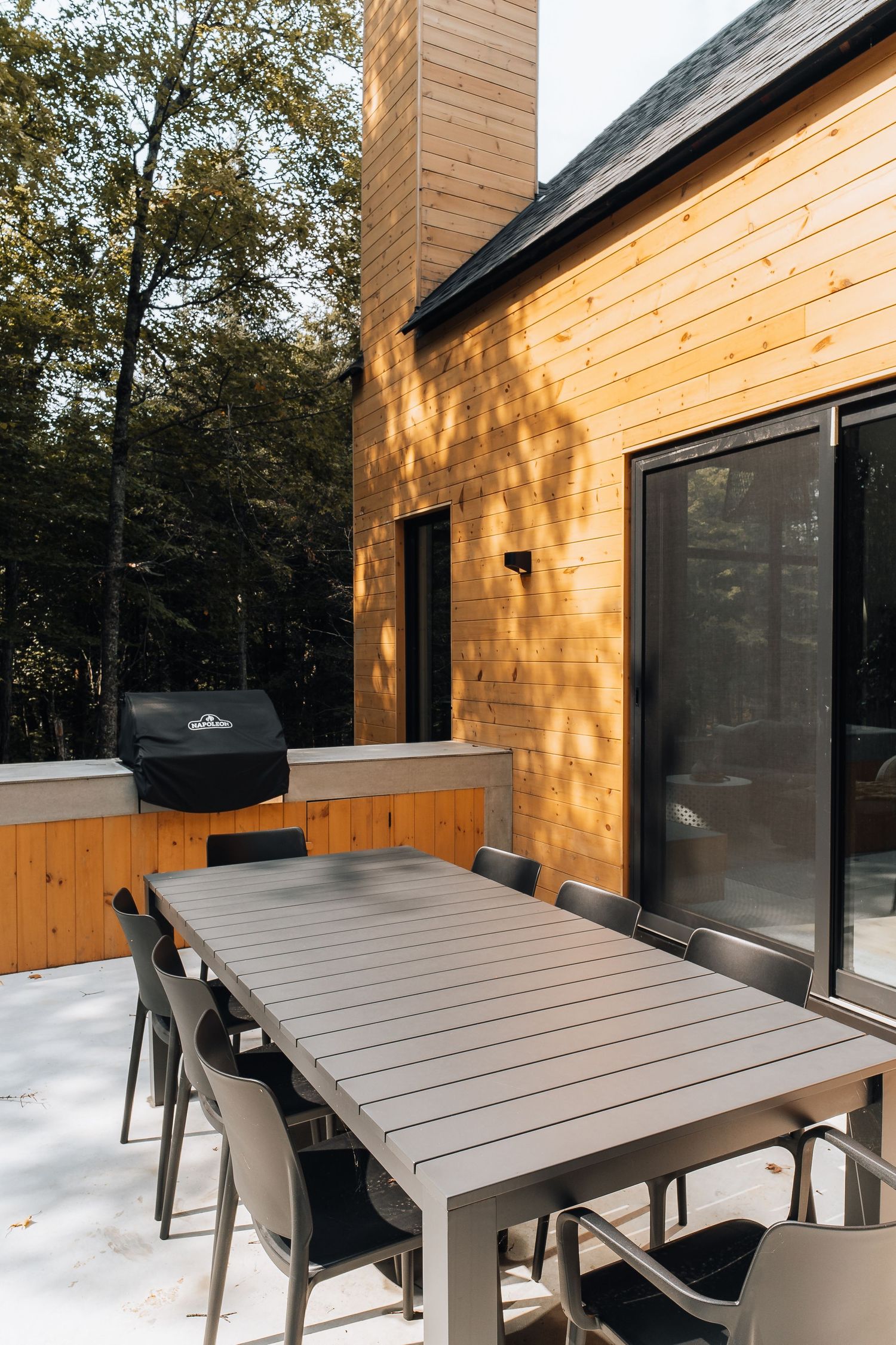 Outdoor dining area with grey table and chairs on wooden deck beside modern cabin.