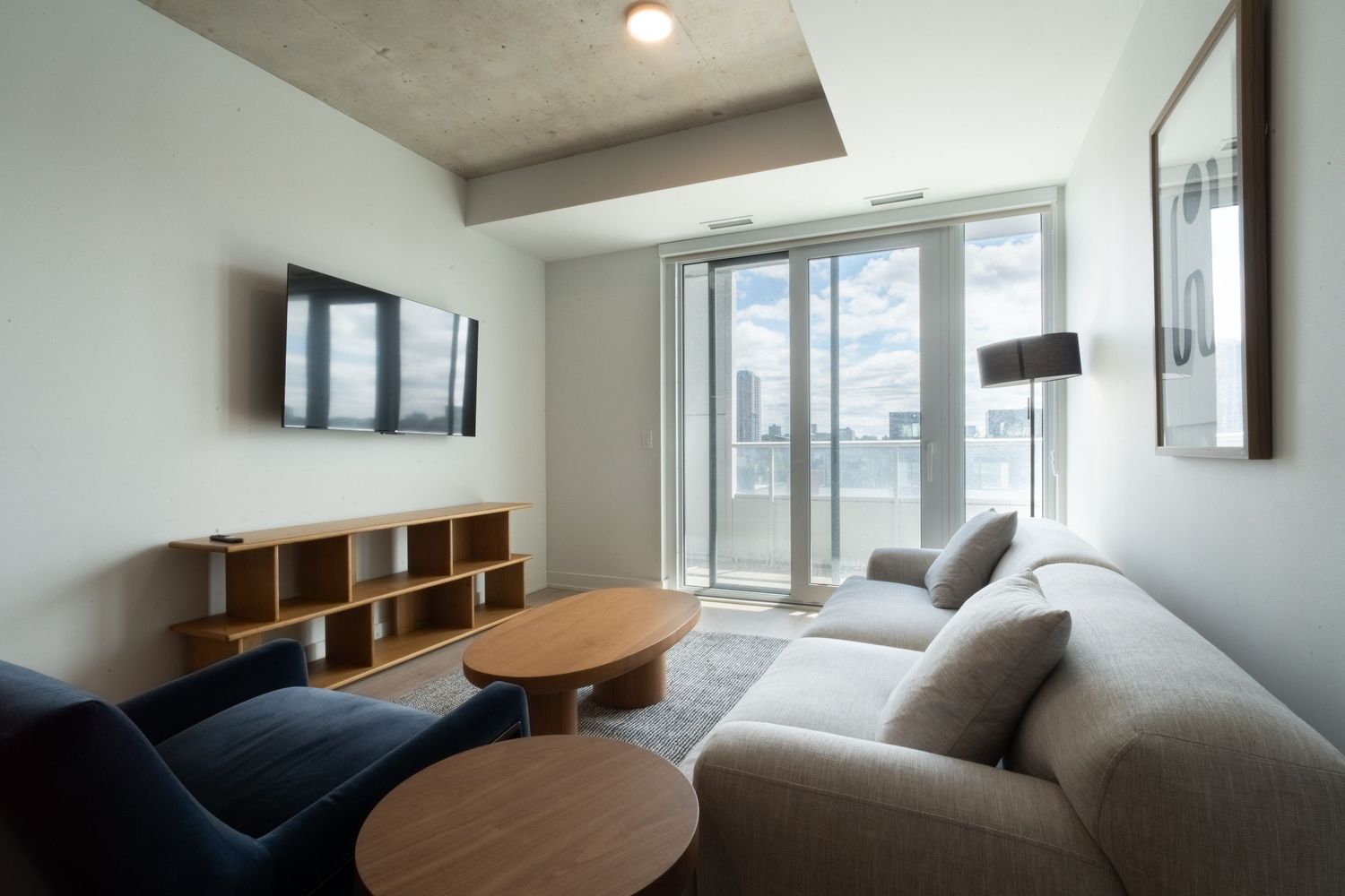 Spacious contemporary living area with natural light and wooden furniture against white walls.