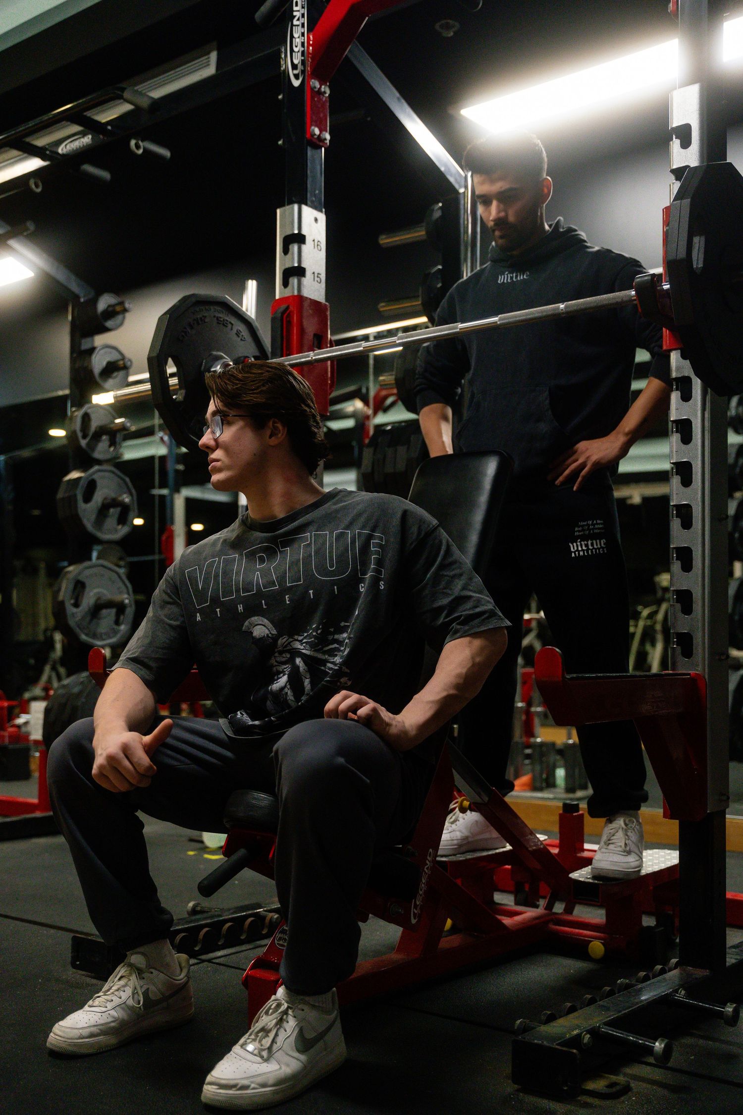Side profile of someone resting between sets on gym equipment in dark lighting.