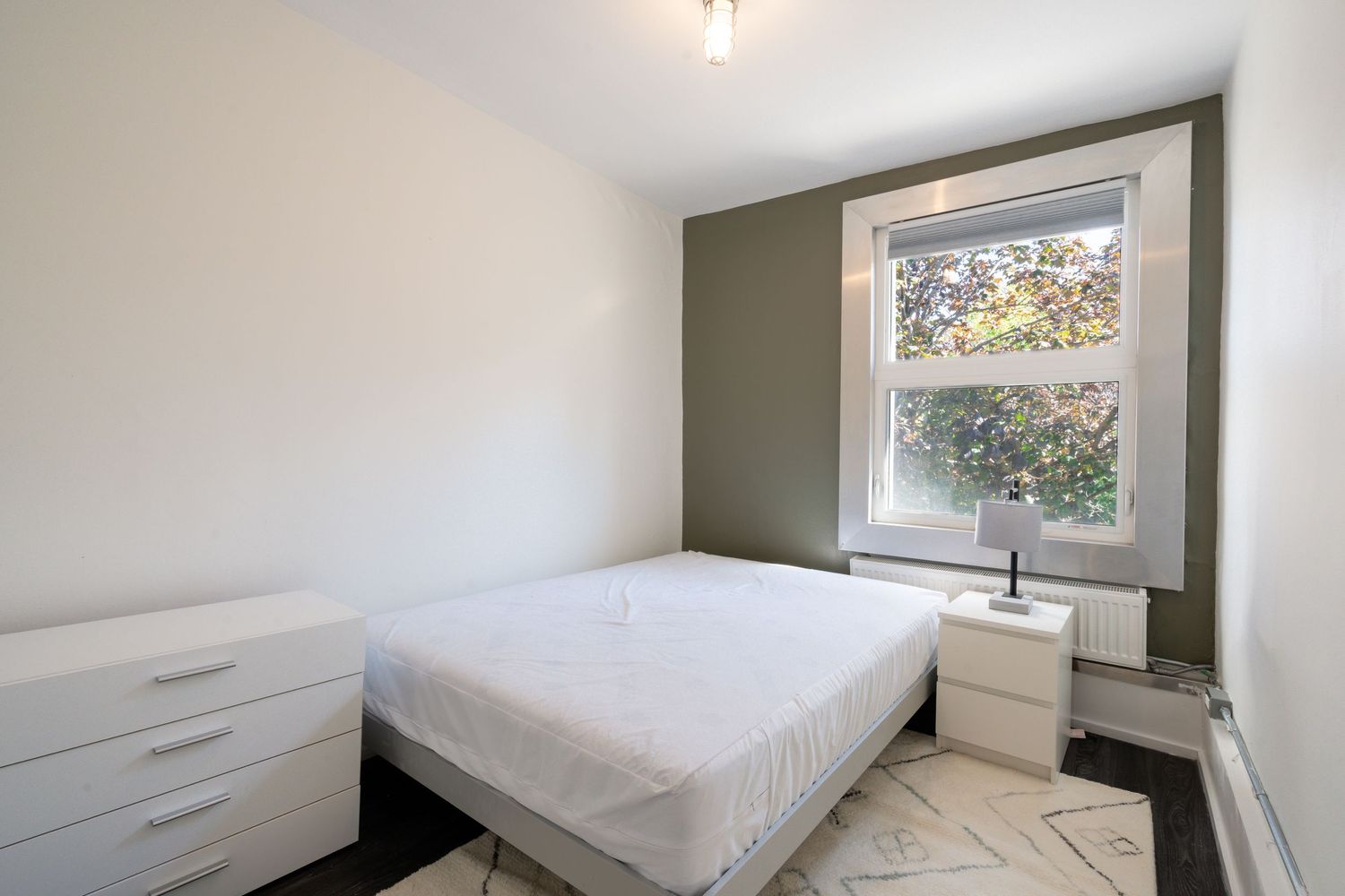 Bright bedroom with white furniture and natural light from window.