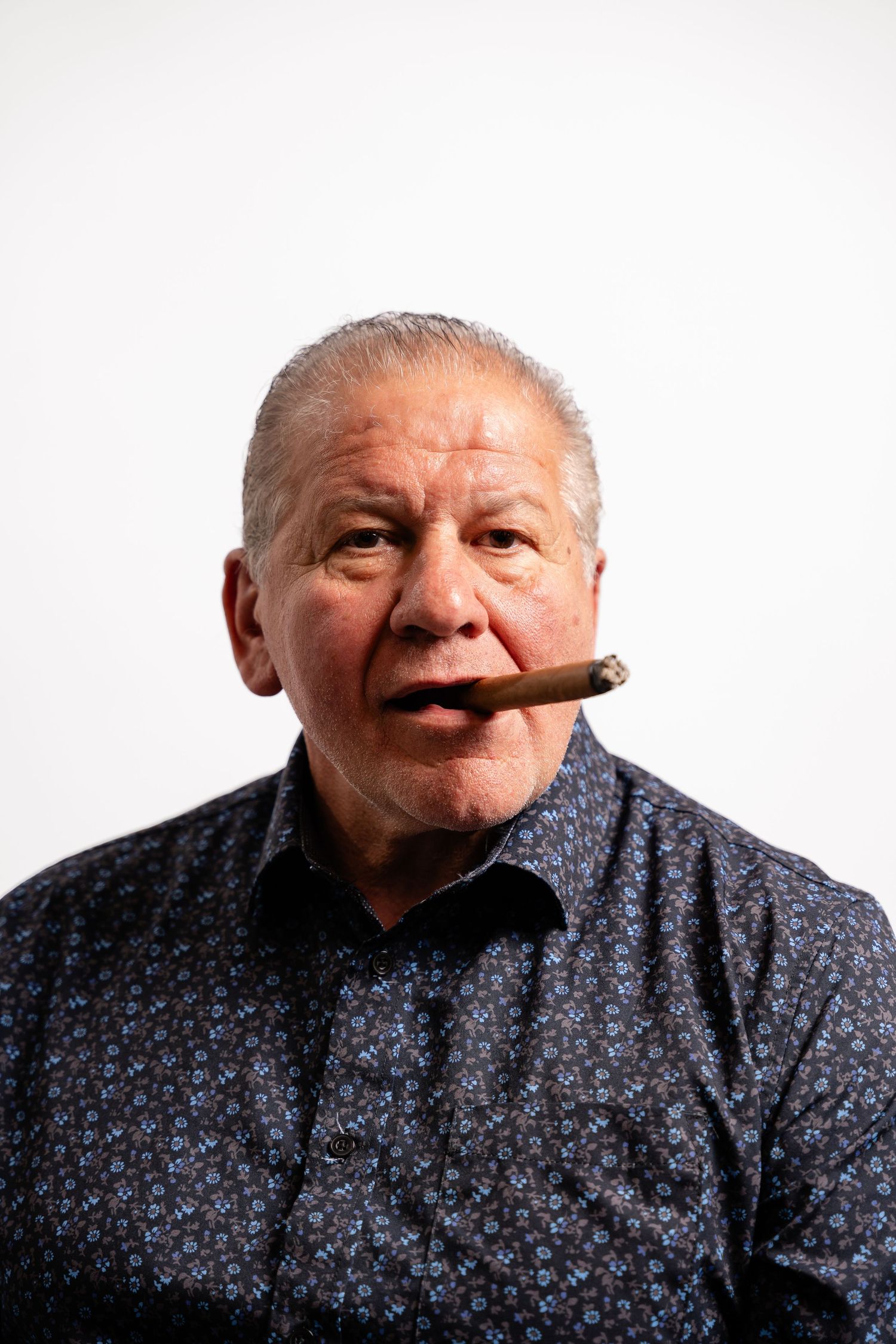 Portrait of person in patterned shirt smoking cigar against white background.