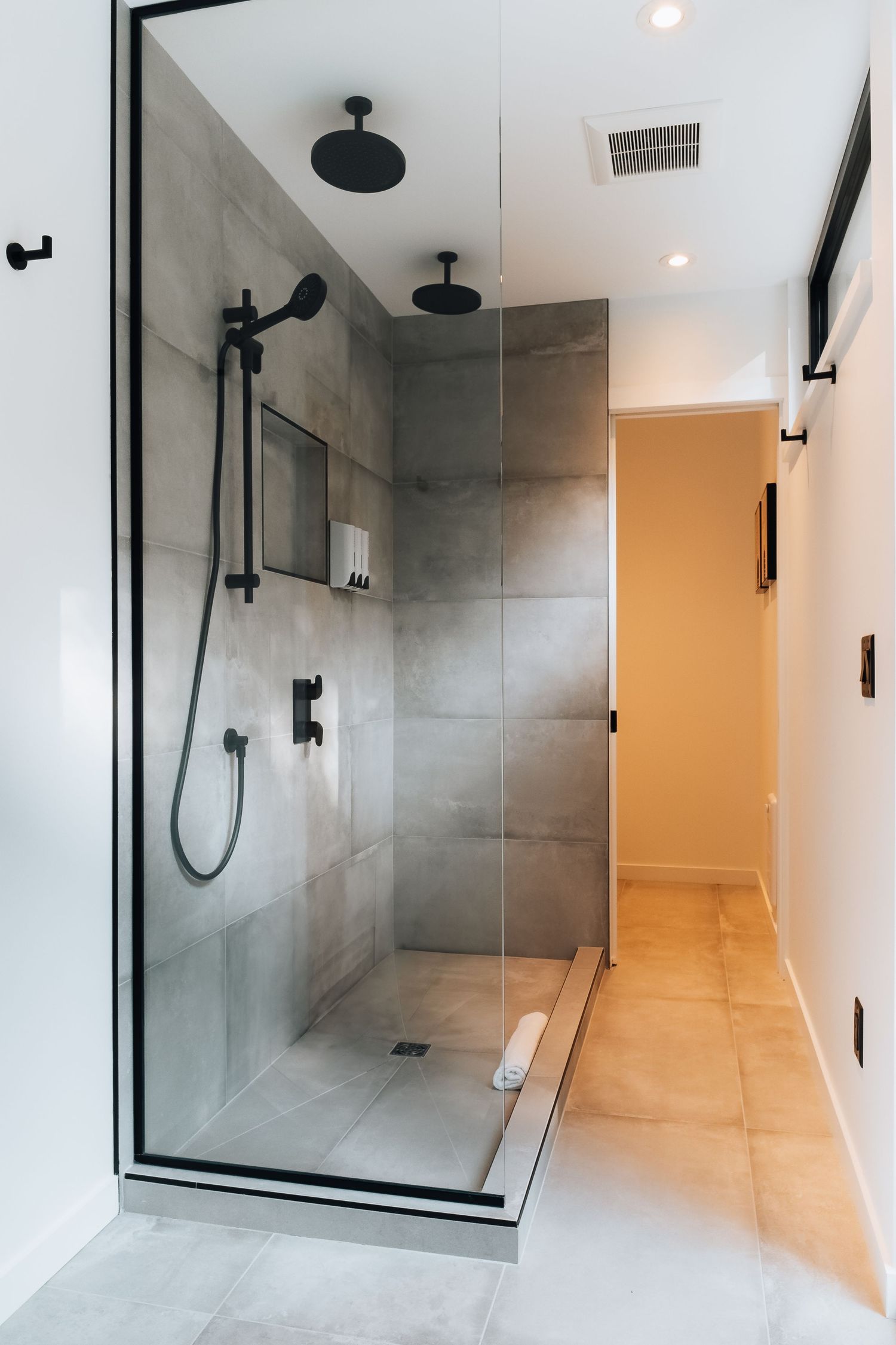 Modern bathroom with glass shower enclosure, grey tiles, and matte black fixtures.