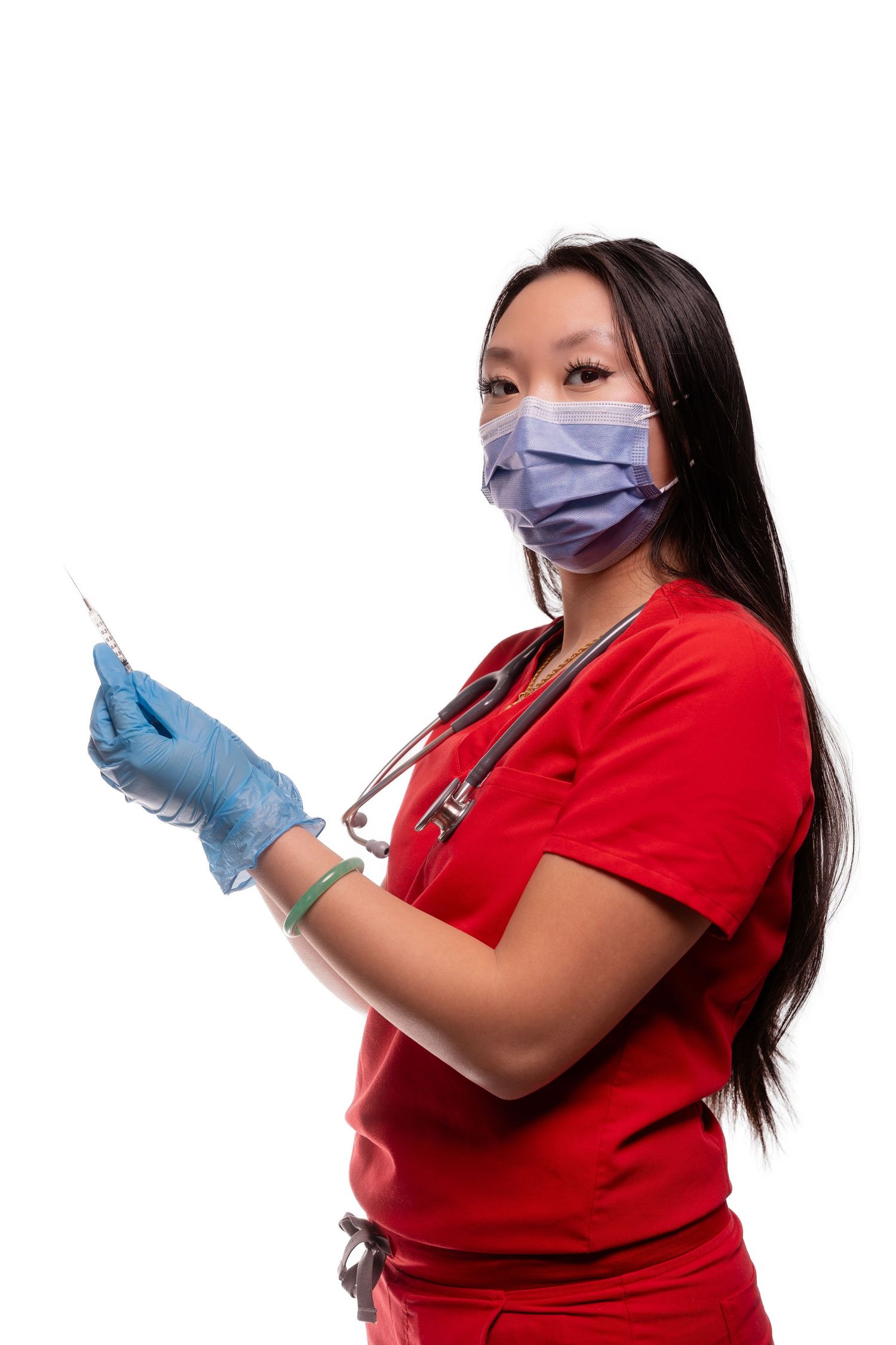 Healthcare worker in red scrubs holds medical syringe while wearing protective equipment.