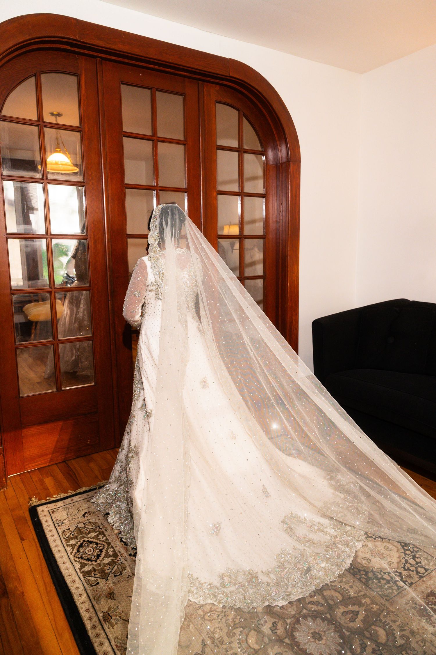 A flowing white lace wedding veil with intricate details draped over wooden furniture in a room with arched doorways.