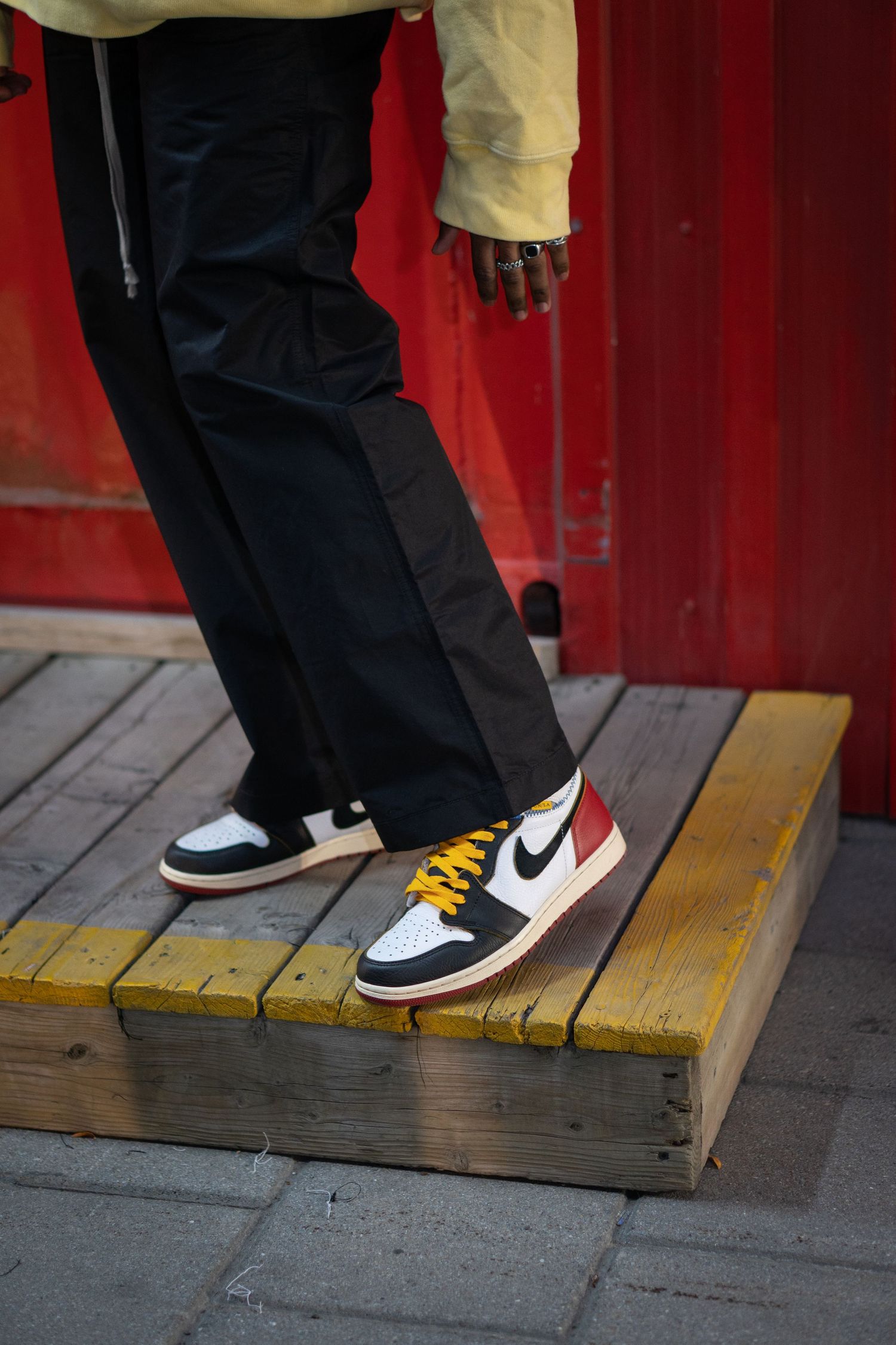 Person wearing black pants and Nike sneakers stepping on yellow wooden platform.