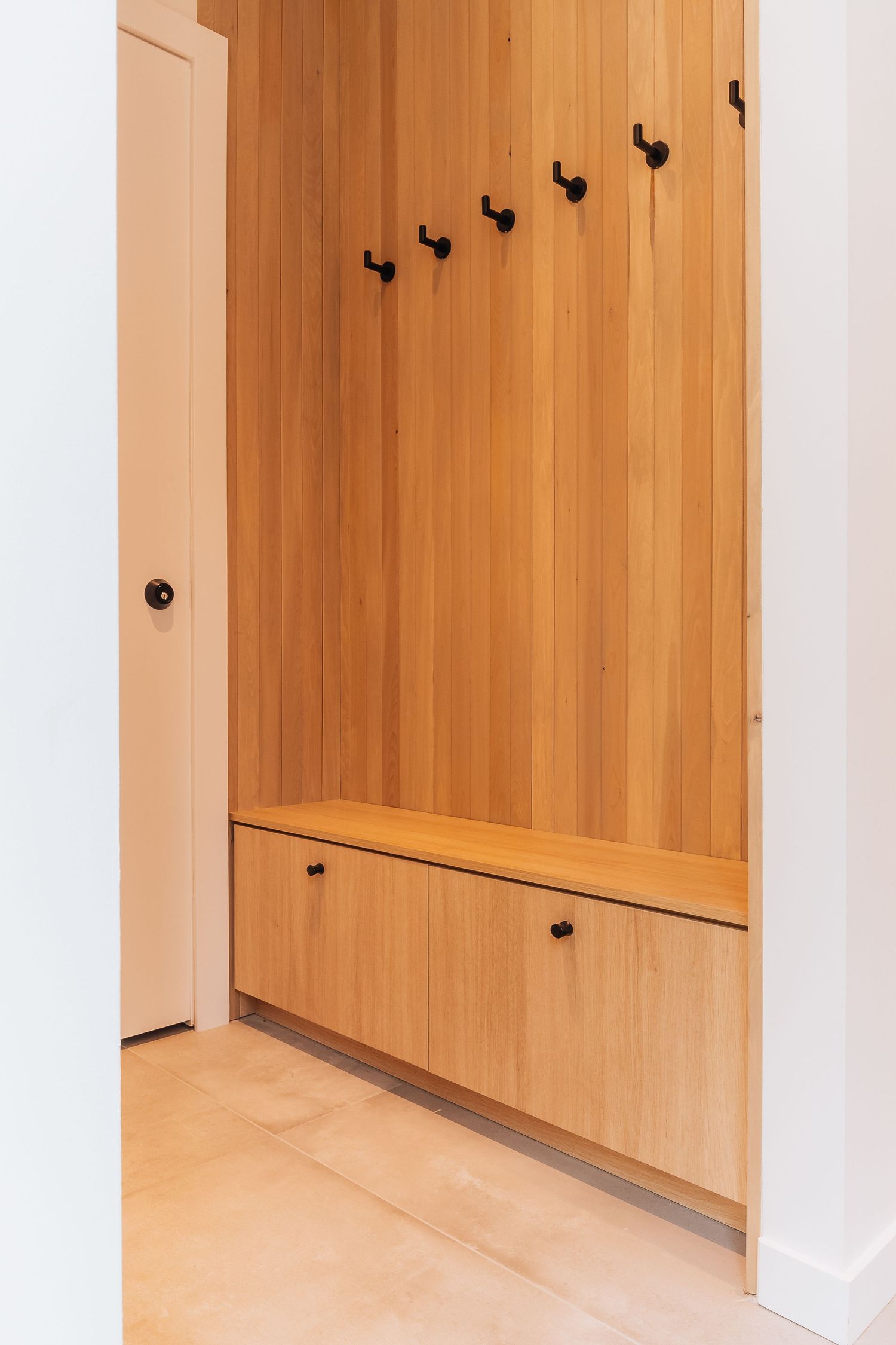 Wood-paneled entryway with black coat hooks features minimalist design and warm tones.