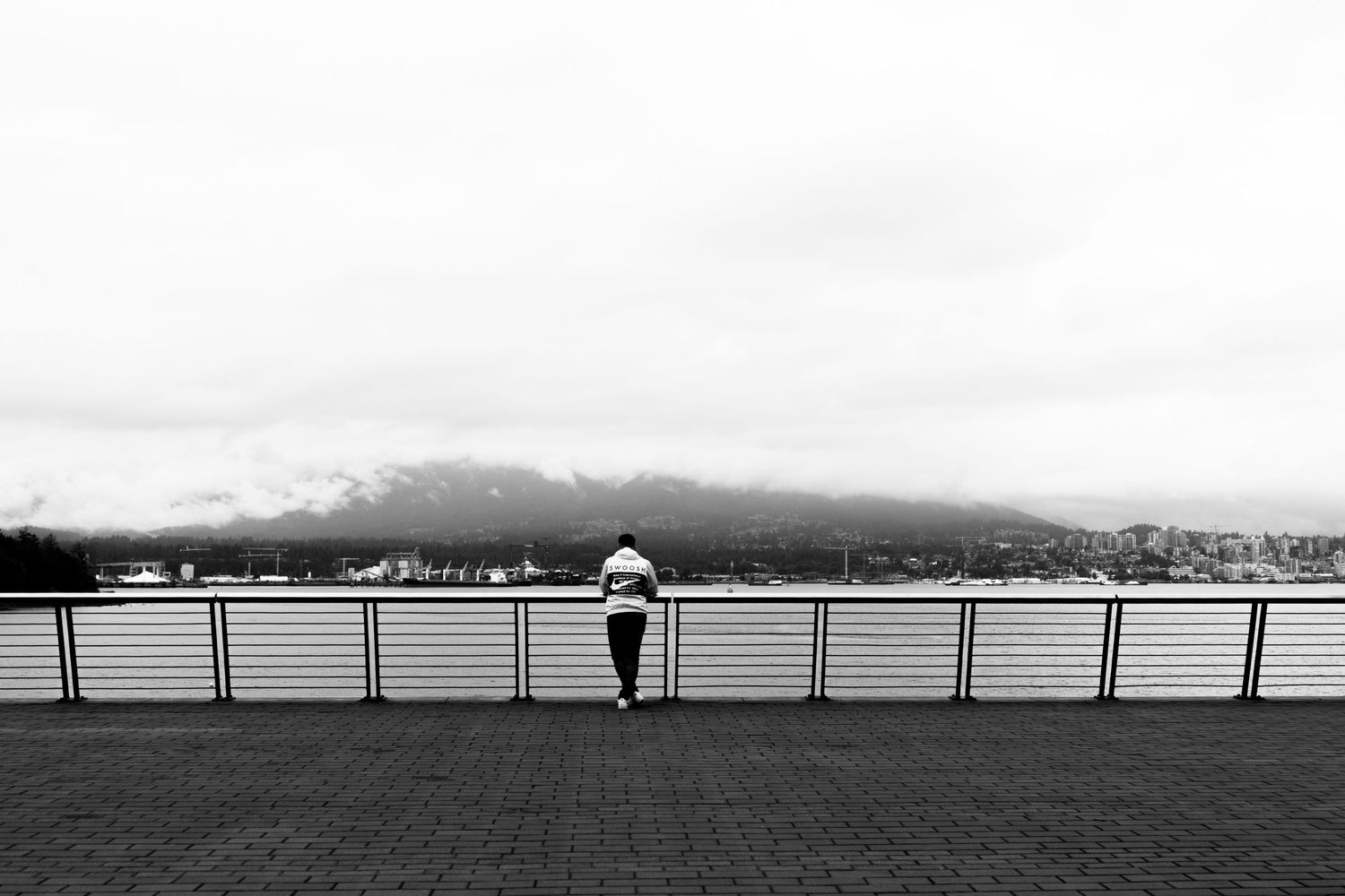Minimalist black and white panoramic landscape with distant figure on railing.
