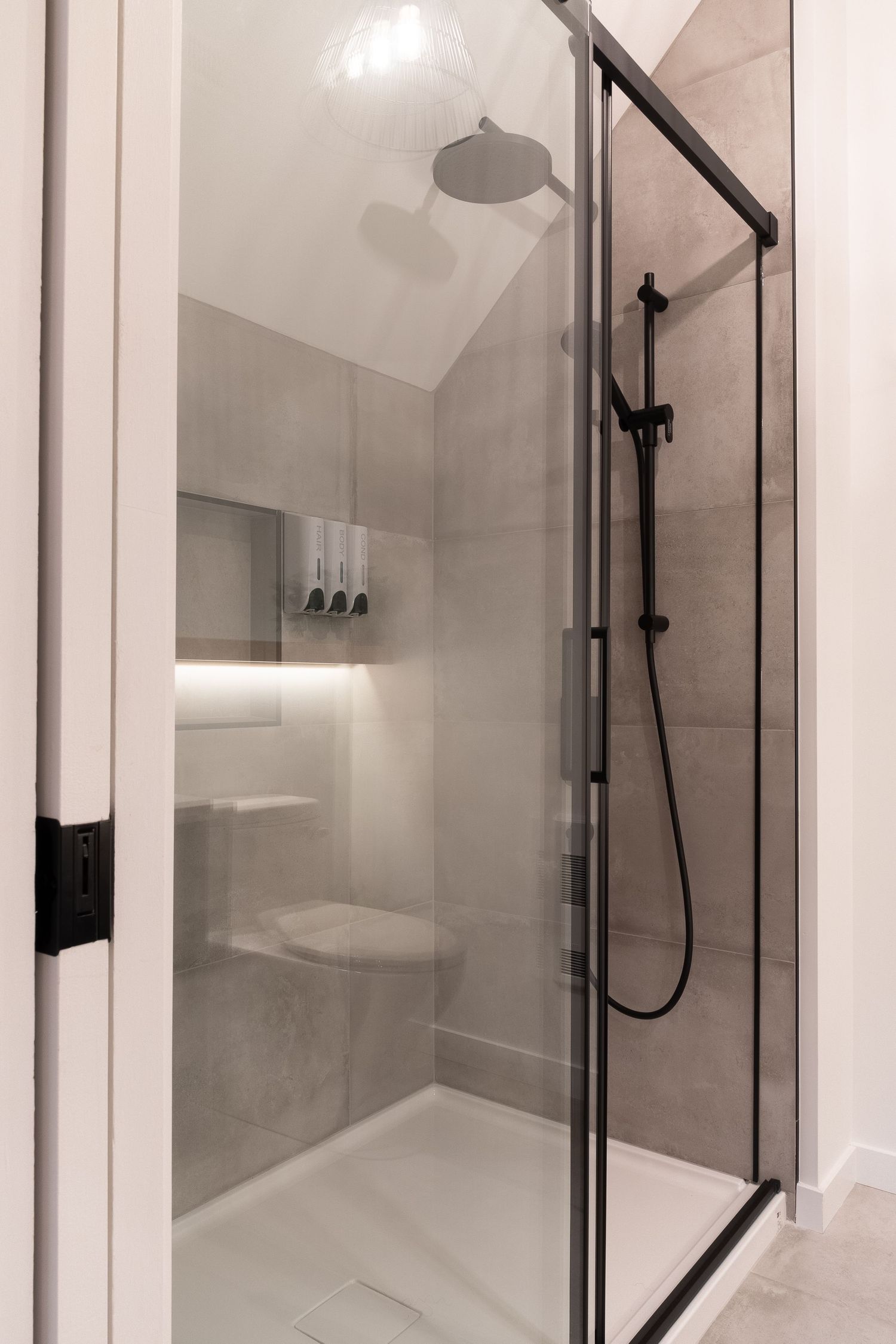 Glass shower enclosure with black frame and rainfall showerhead in modern bathroom.