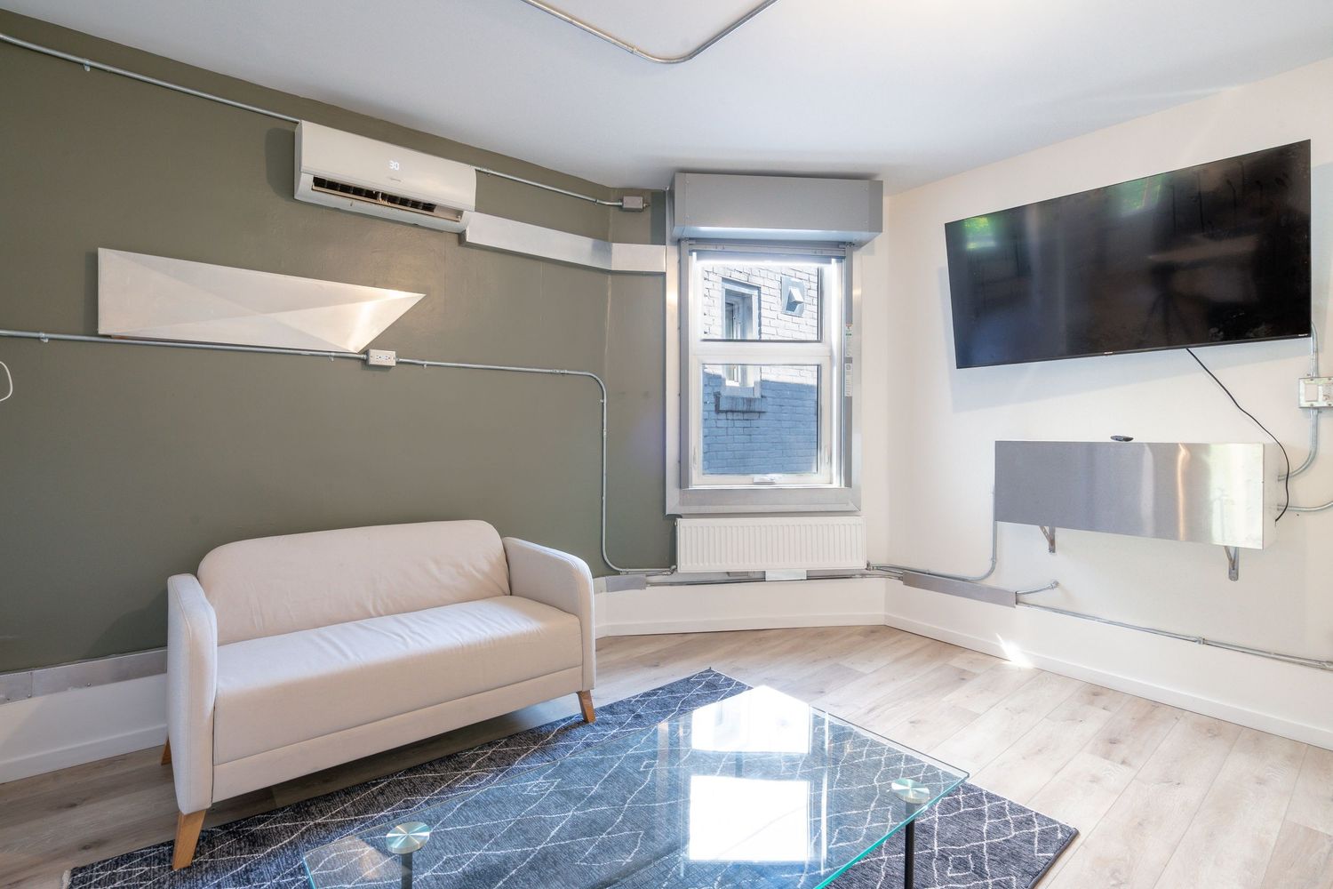 Contemporary basement living space with gray walls, mounted TV, and natural light from window wells.