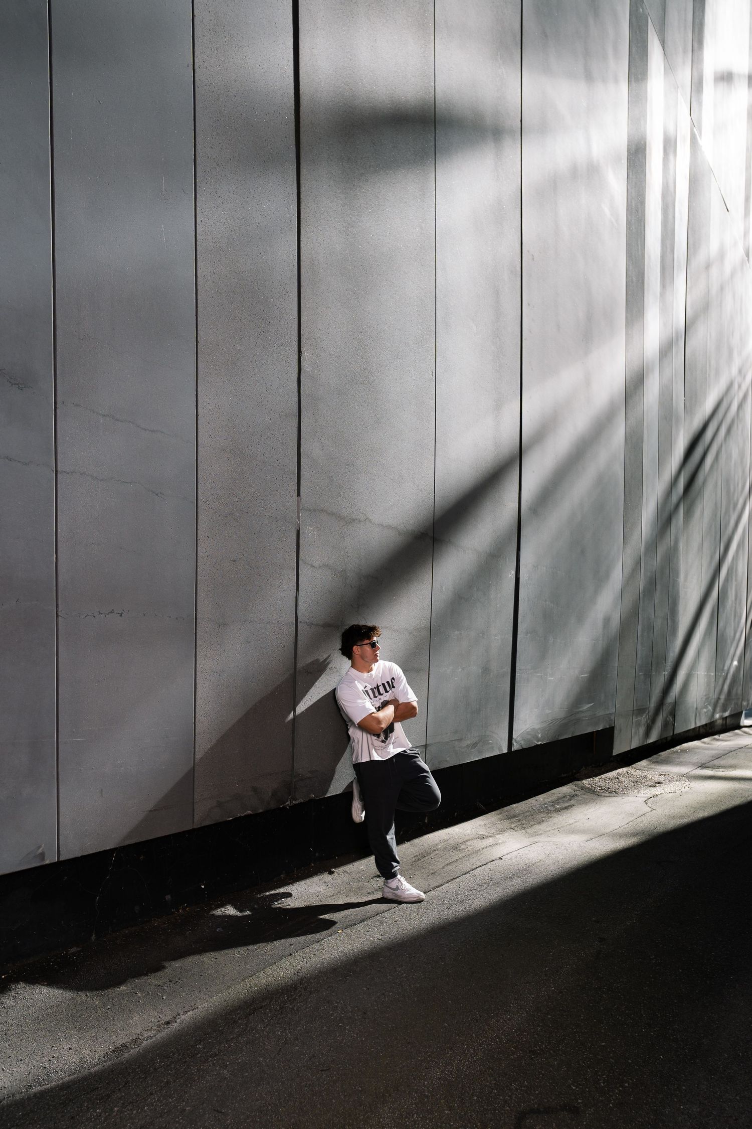Dynamic street fashion photo with dramatic shadows and concrete wall.