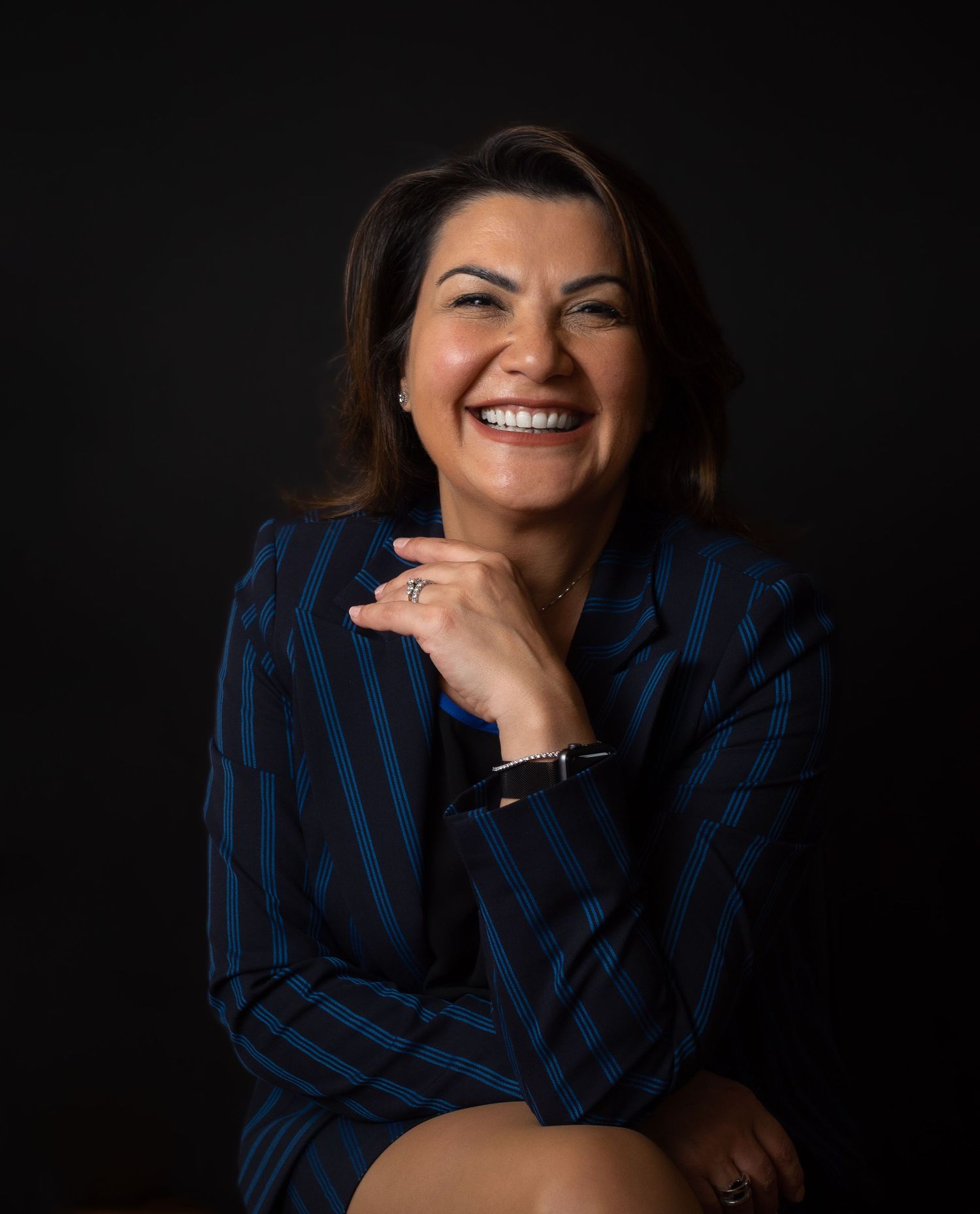 Professional portrait of person in striped blazer smiling against dark background.