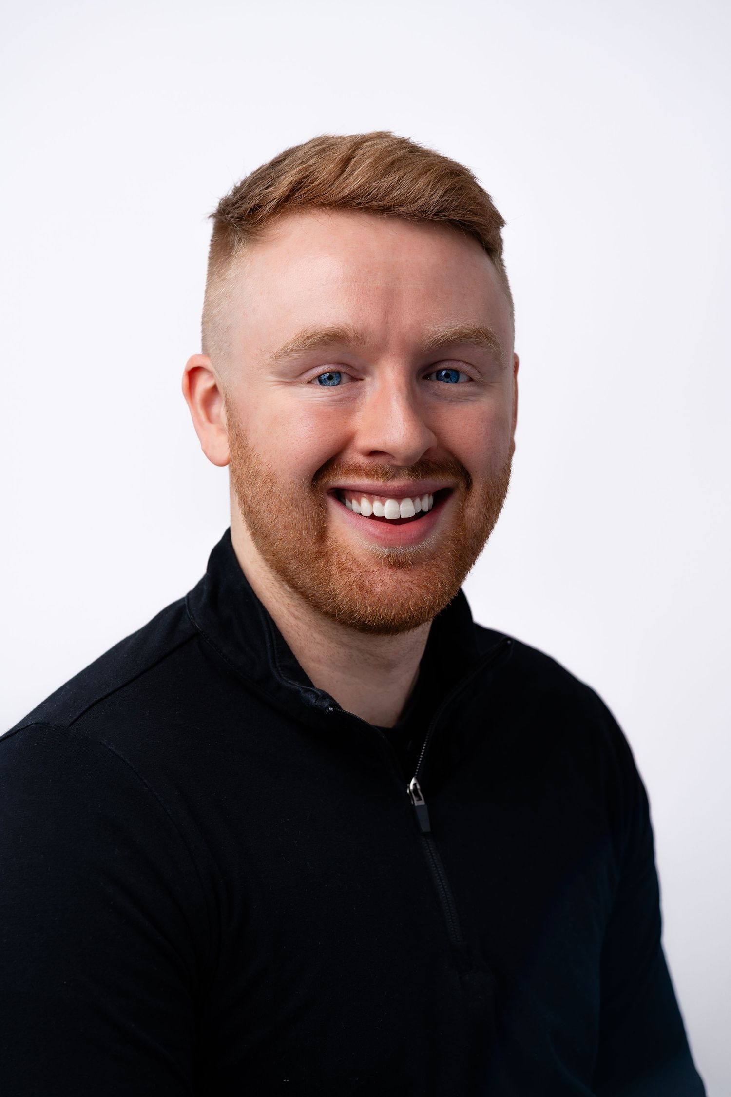 Professional headshot of person in black quarter-zip sweater smiling against white background.