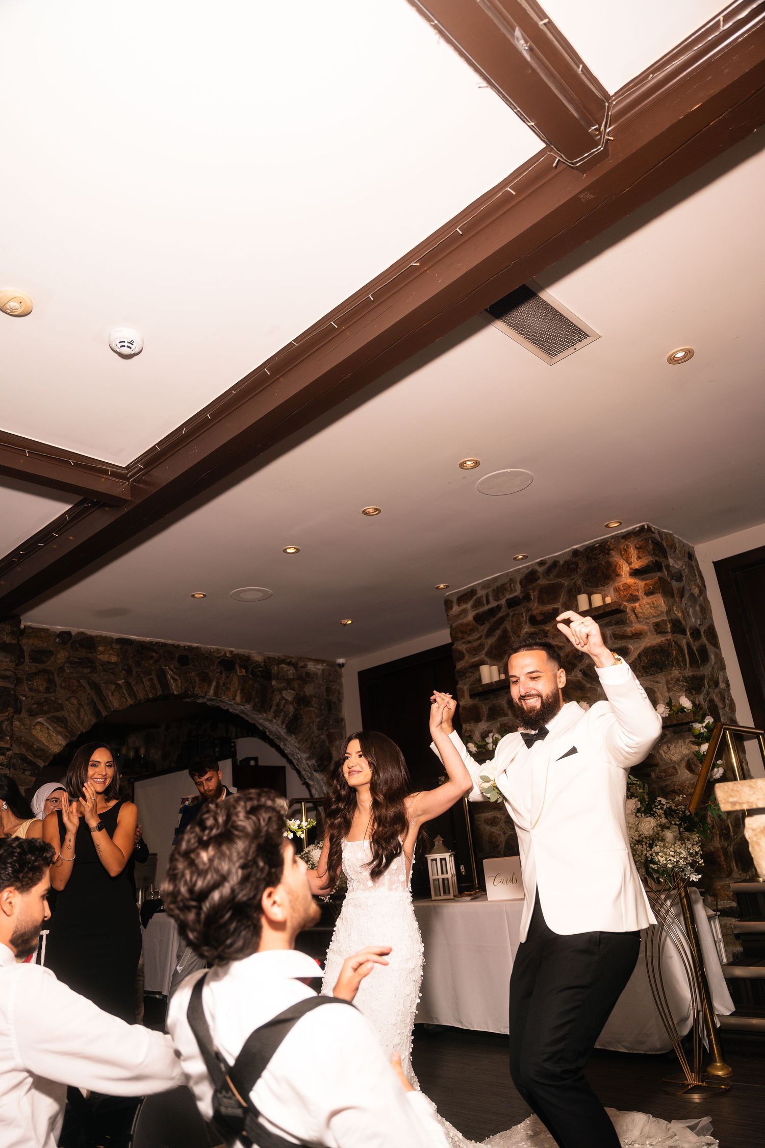 People dancing and celebrating in a room with exposed wooden beams and white ceiling.