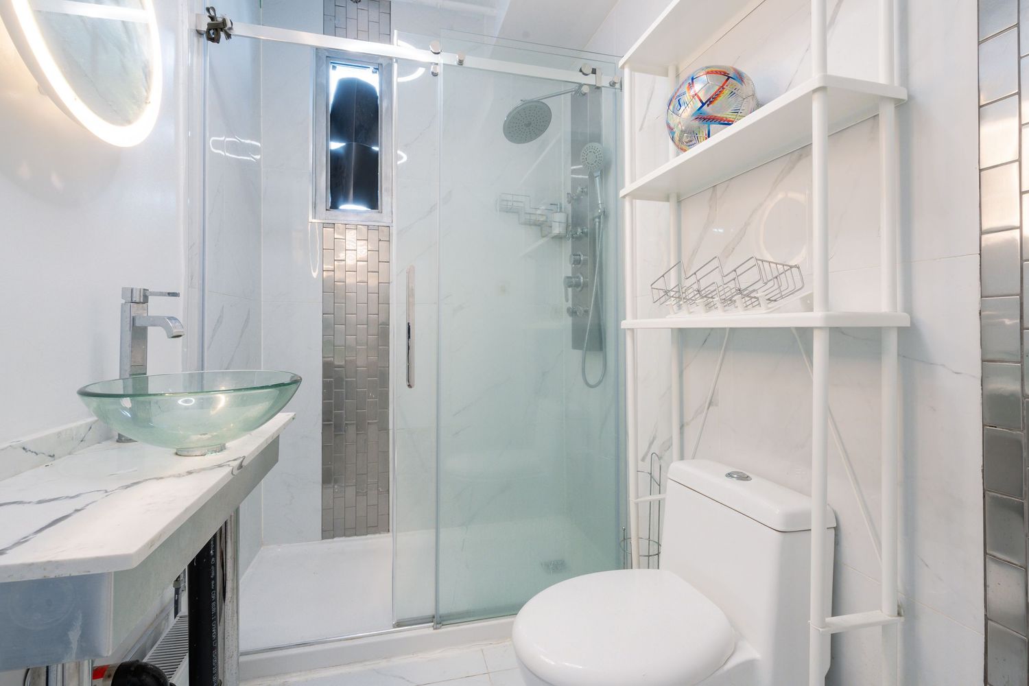 Sleek modern bathroom with glass shower enclosure and white marble-look tiles.