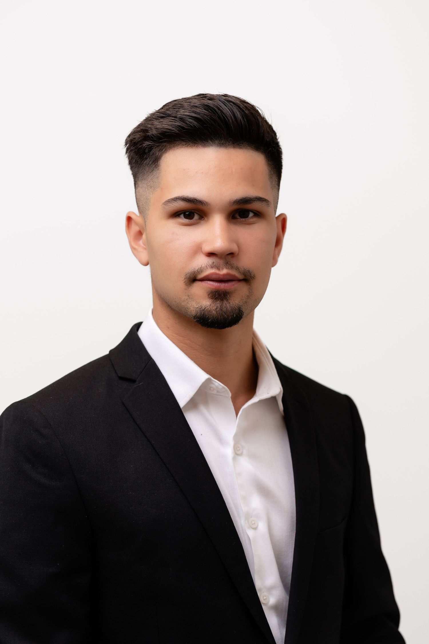 Professional portrait of young man in black suit and white shirt against white background.