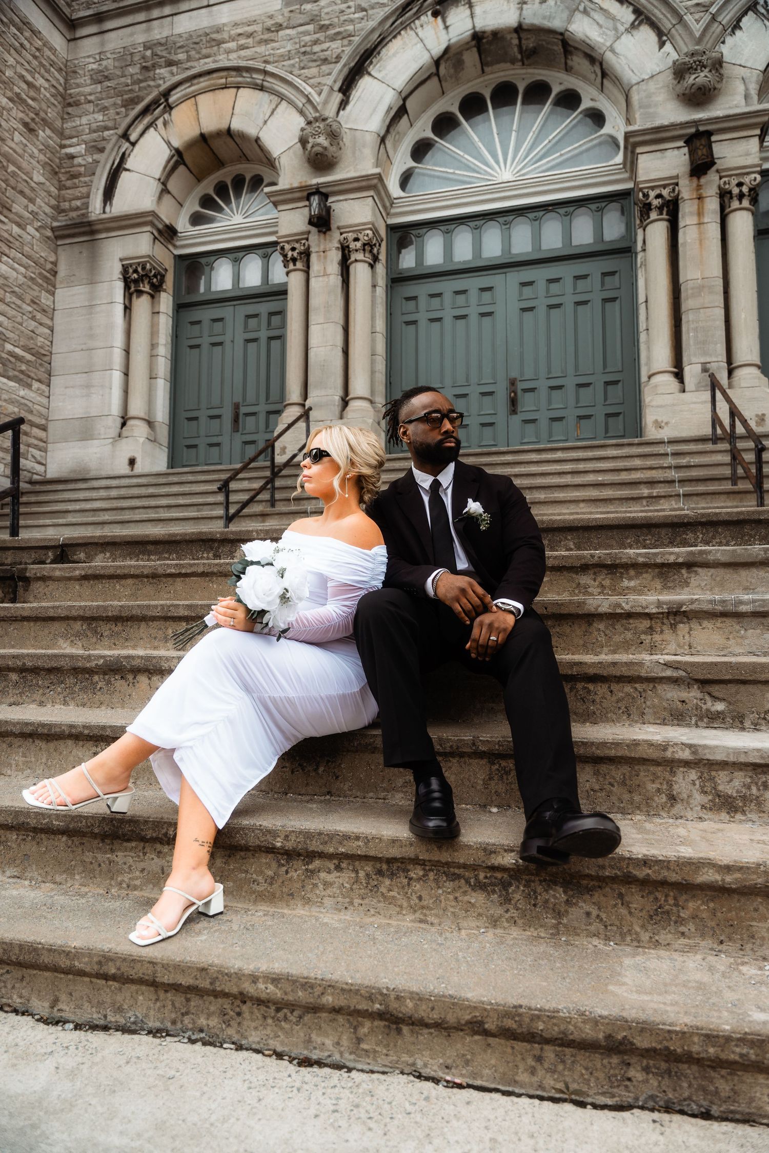 Bride and groom sit casually on historic stone steps during wedding photoshoot.