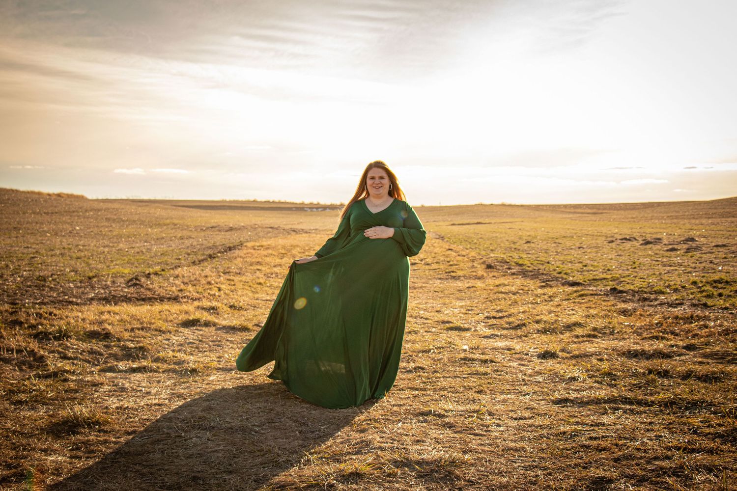 Expectant mother in flowing dress at sunset in open field