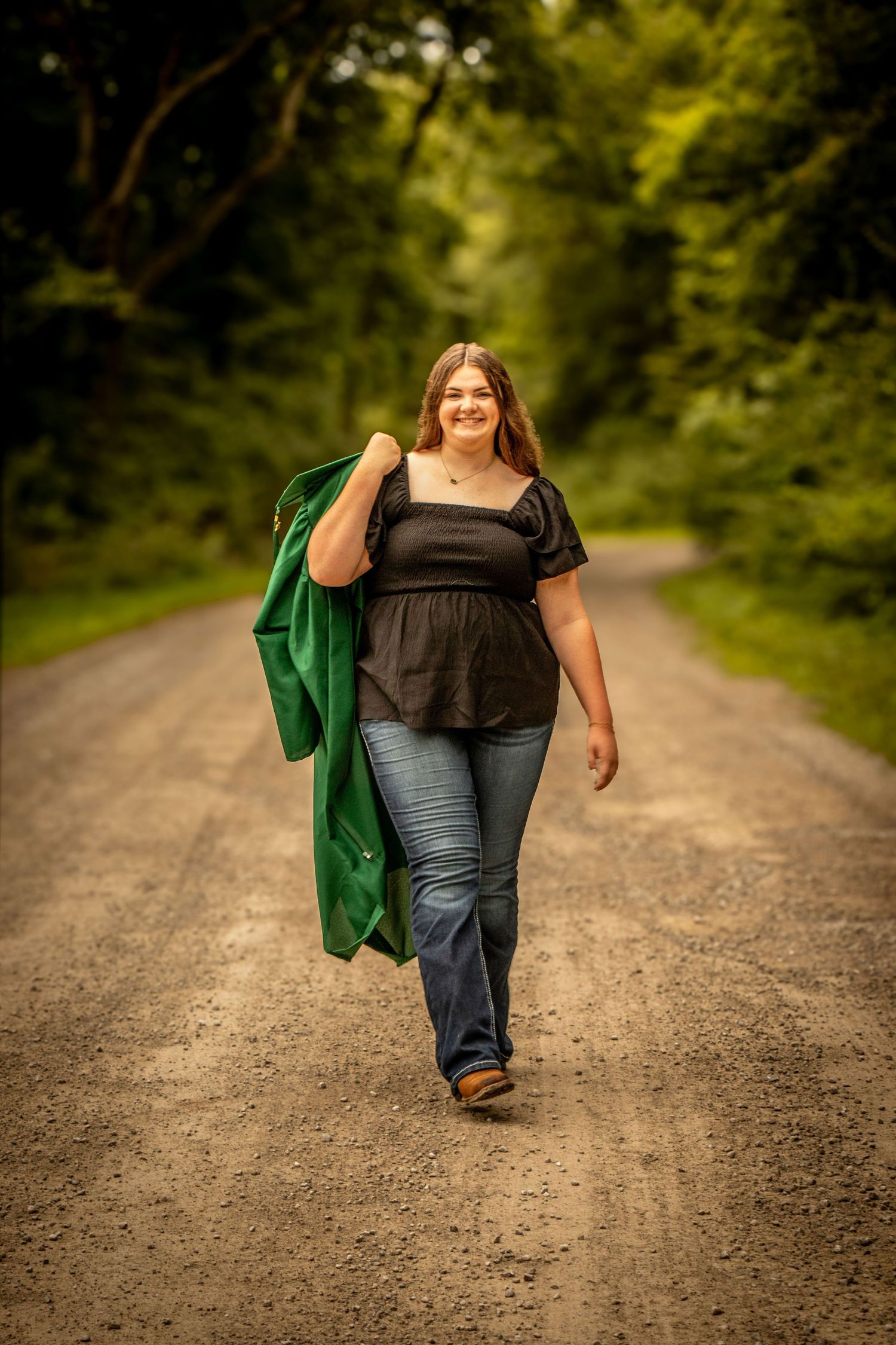 Senior girl with graduation gown on gravel road