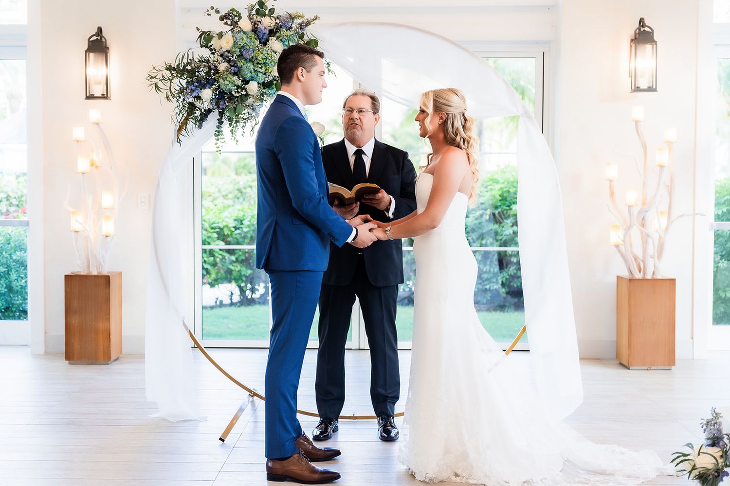 Indoor wedding ceremony space with white pillars, elegant lighting, and natural window views.