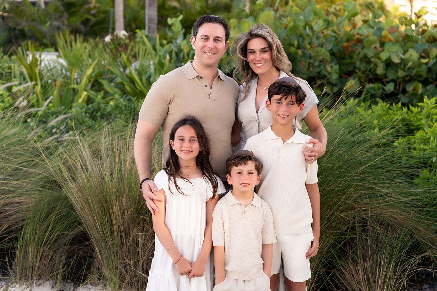 A family of four dressed in coordinating cream and beige outfits posing in a garden setting.
