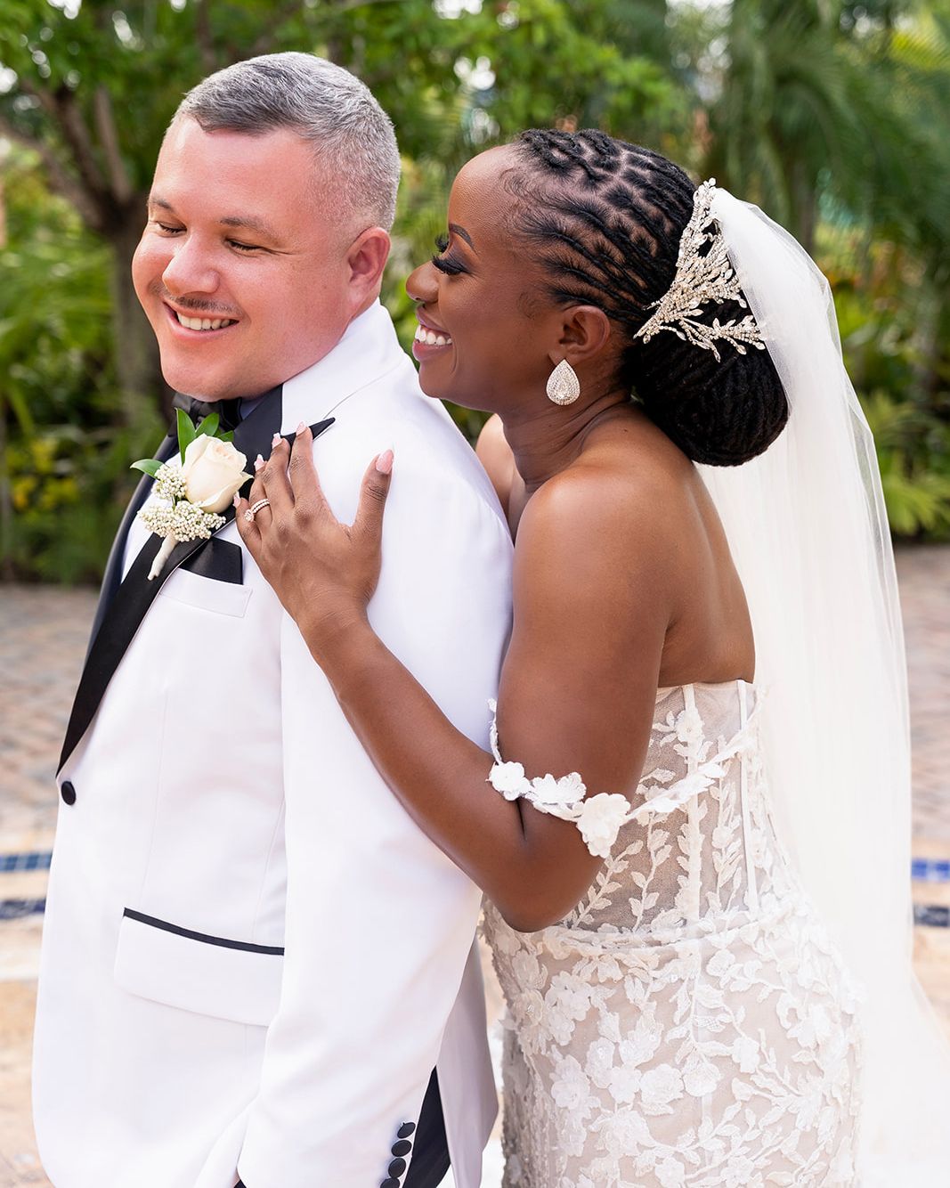 A joyful moment between newlyweds in their wedding attire, with the bride in a lace gown and the groom in a white tuxedo.
