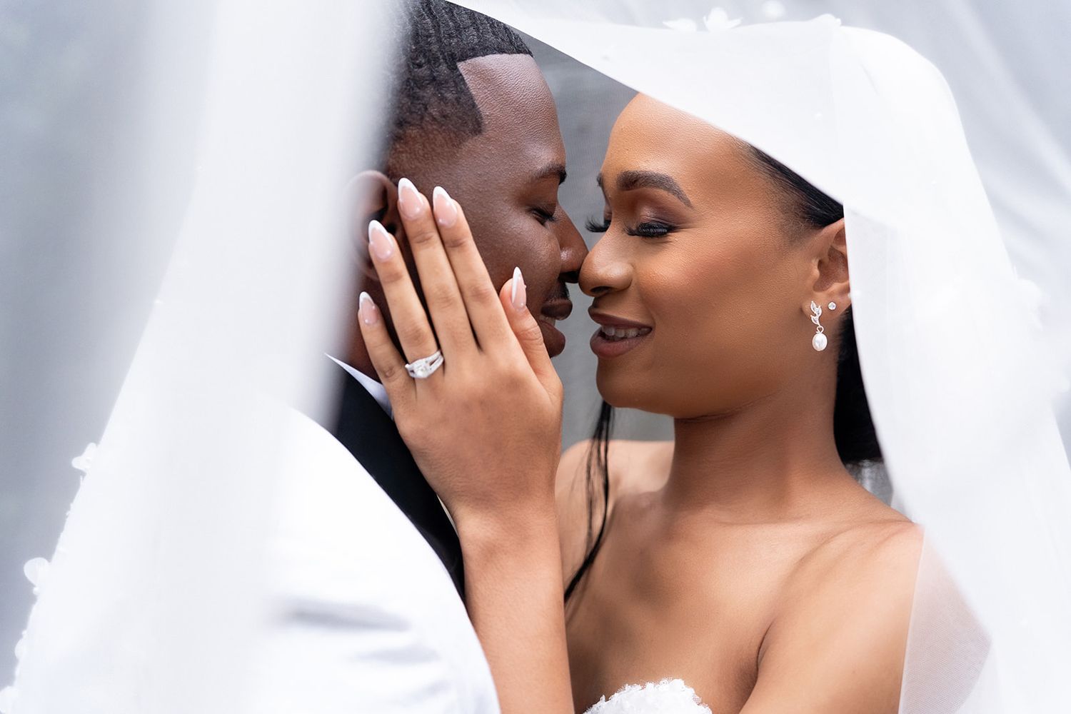 An intimate wedding portrait showing tender embrace between newlyweds under a white veil.