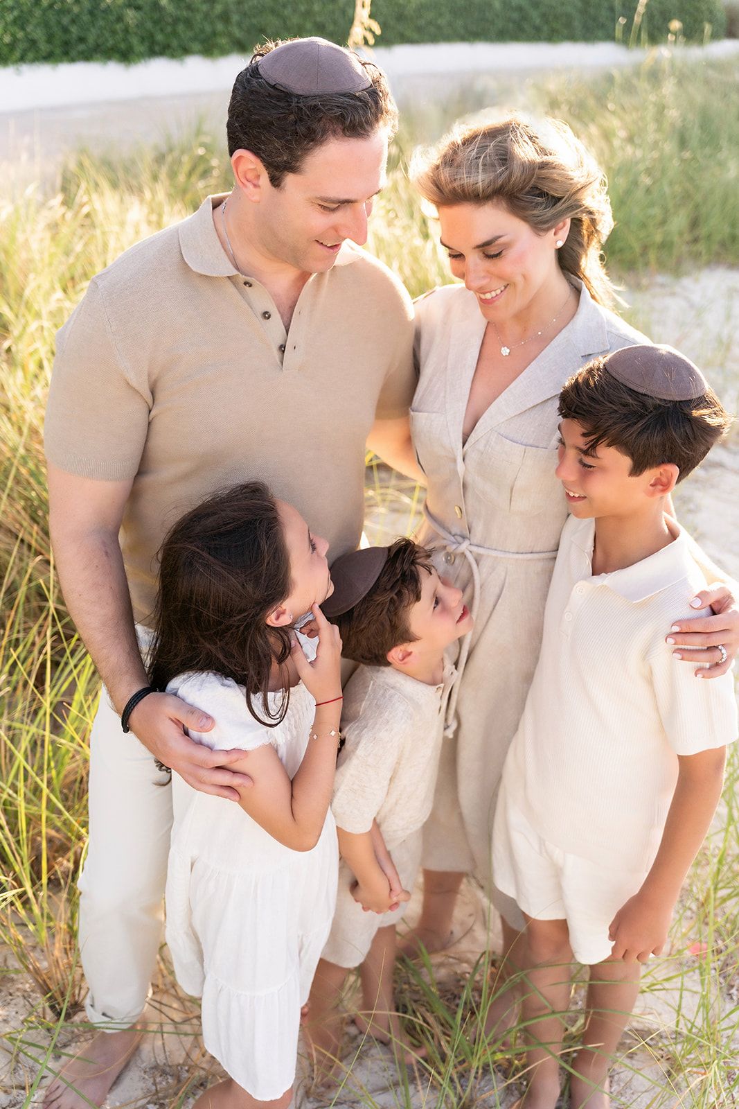 Family wearing neutral colored clothing stands together in golden grass during sunset outdoor portrait session.