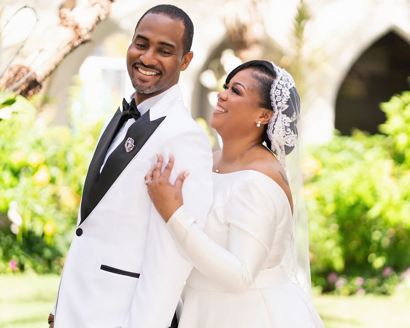 A joyful couple shares a romantic moment together in their wedding attire on a bright sunny day.