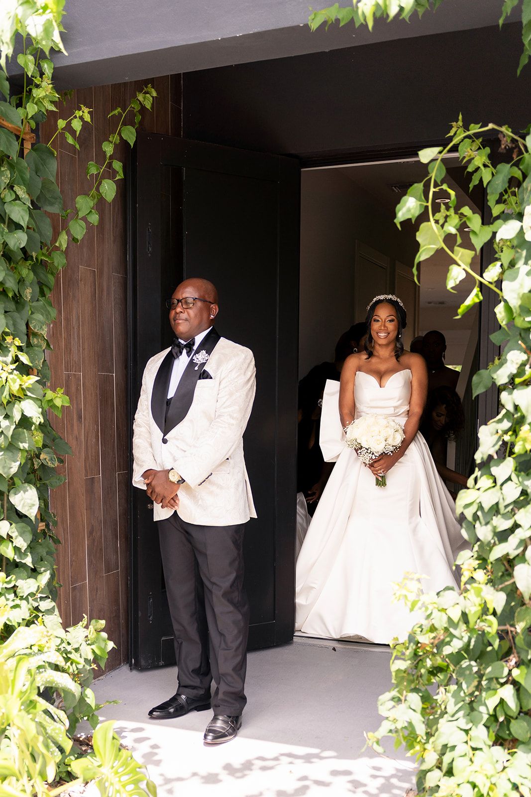 Wedding couple posing amid green ivy vines along white architectural columns.
