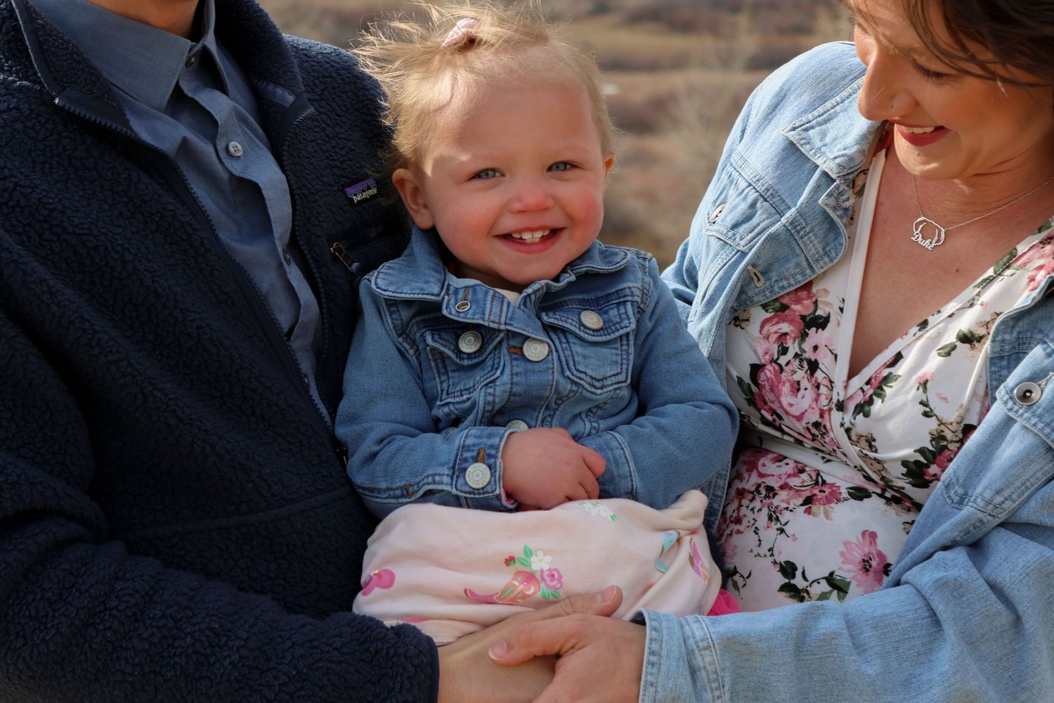 A group of people in denim jackets and floral prints gather together in front of a natural outdoor setting.