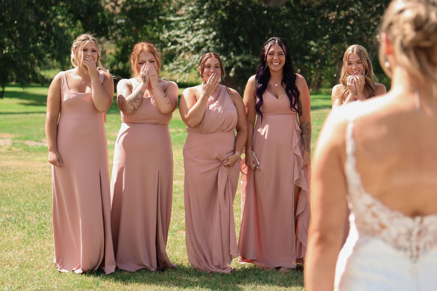 Bridesmaids in matching dusty rose gowns share a joyful first look moment with the bride during an outdoor wedding in Montana.