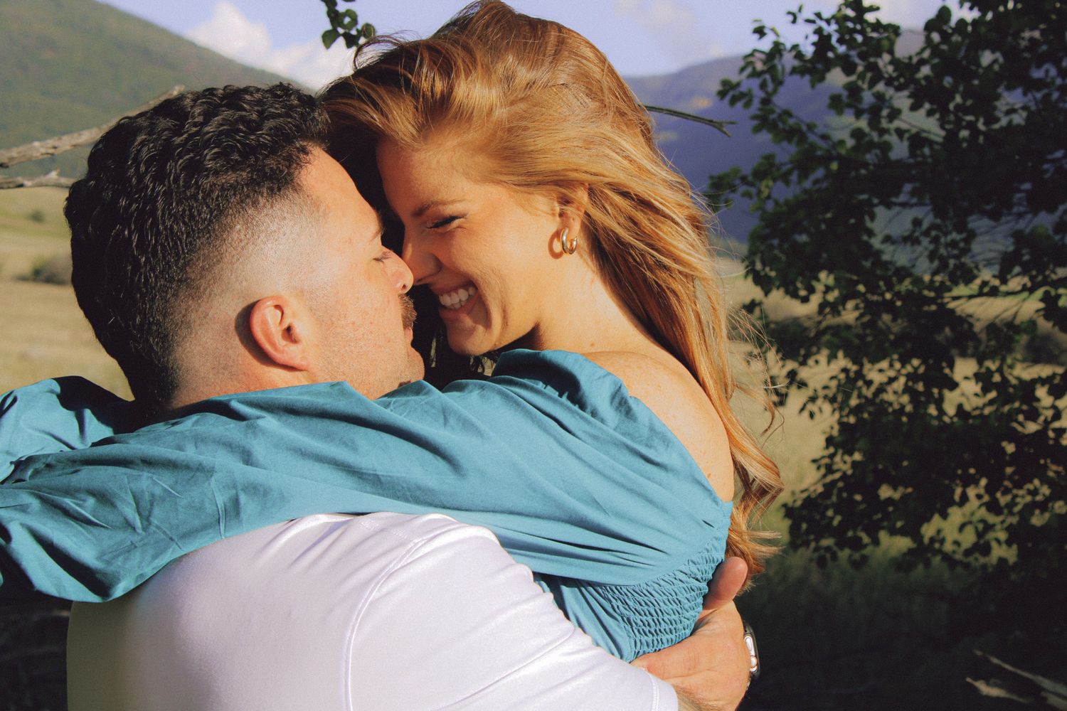 A romantic couple embraces against a Montana mountain landscape background on a sunny day.