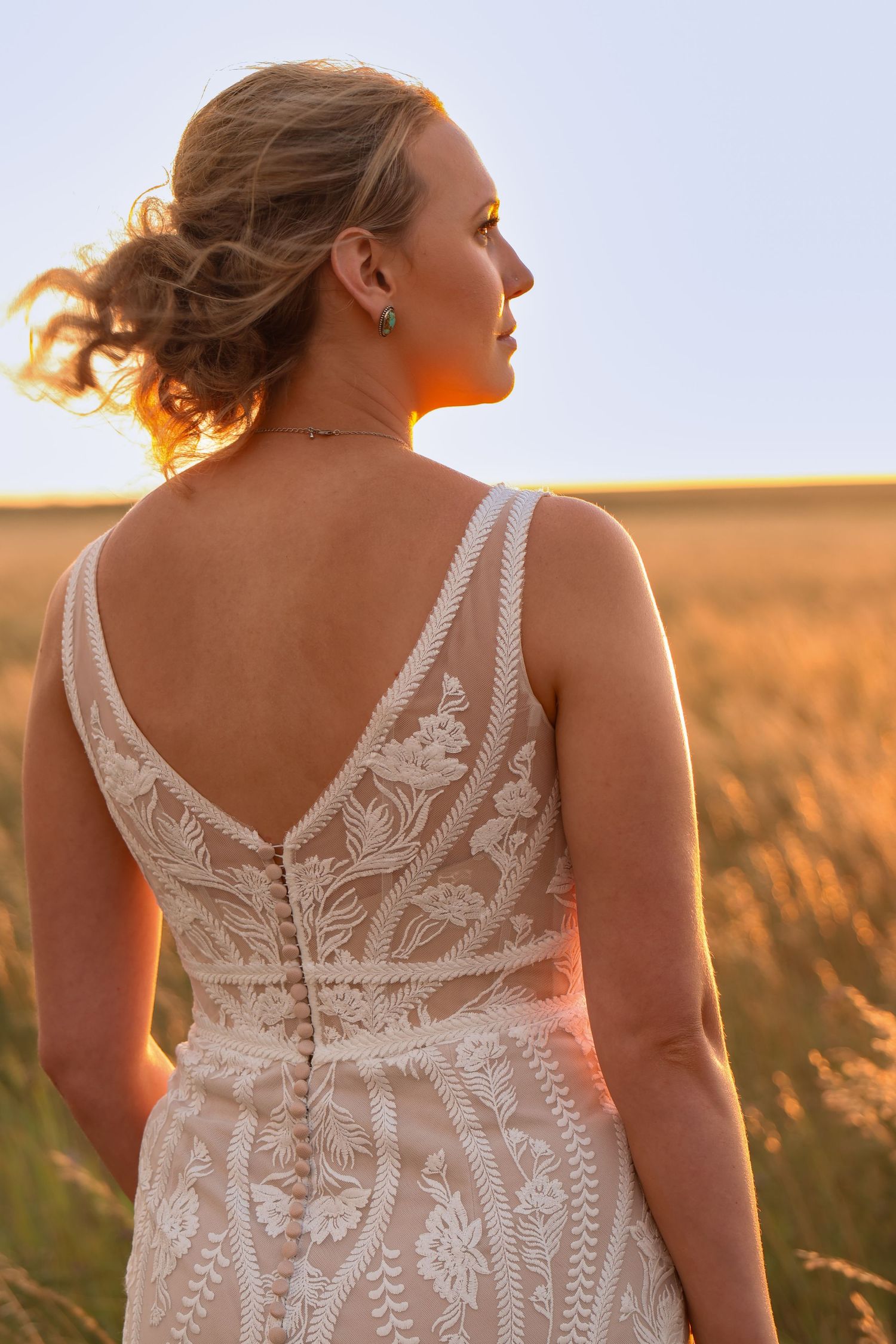 A portrait of a bride in an intricate lace wedding dress during golden hour in a Montana wheat field.