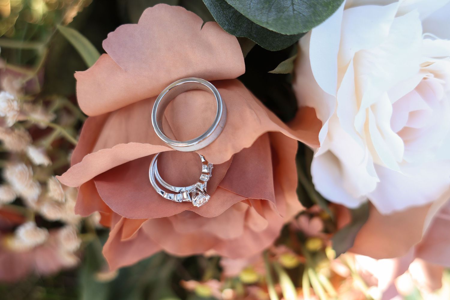 Silver wedding rings nestled on peach and white rose petals in a romantic floral setting.