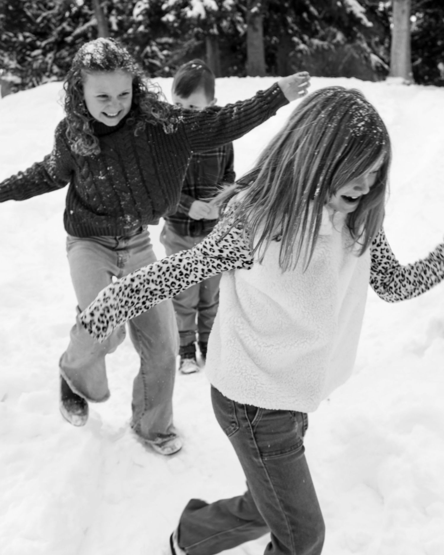 Young people playing and walking through snow together on a winter day, captured in black and white.