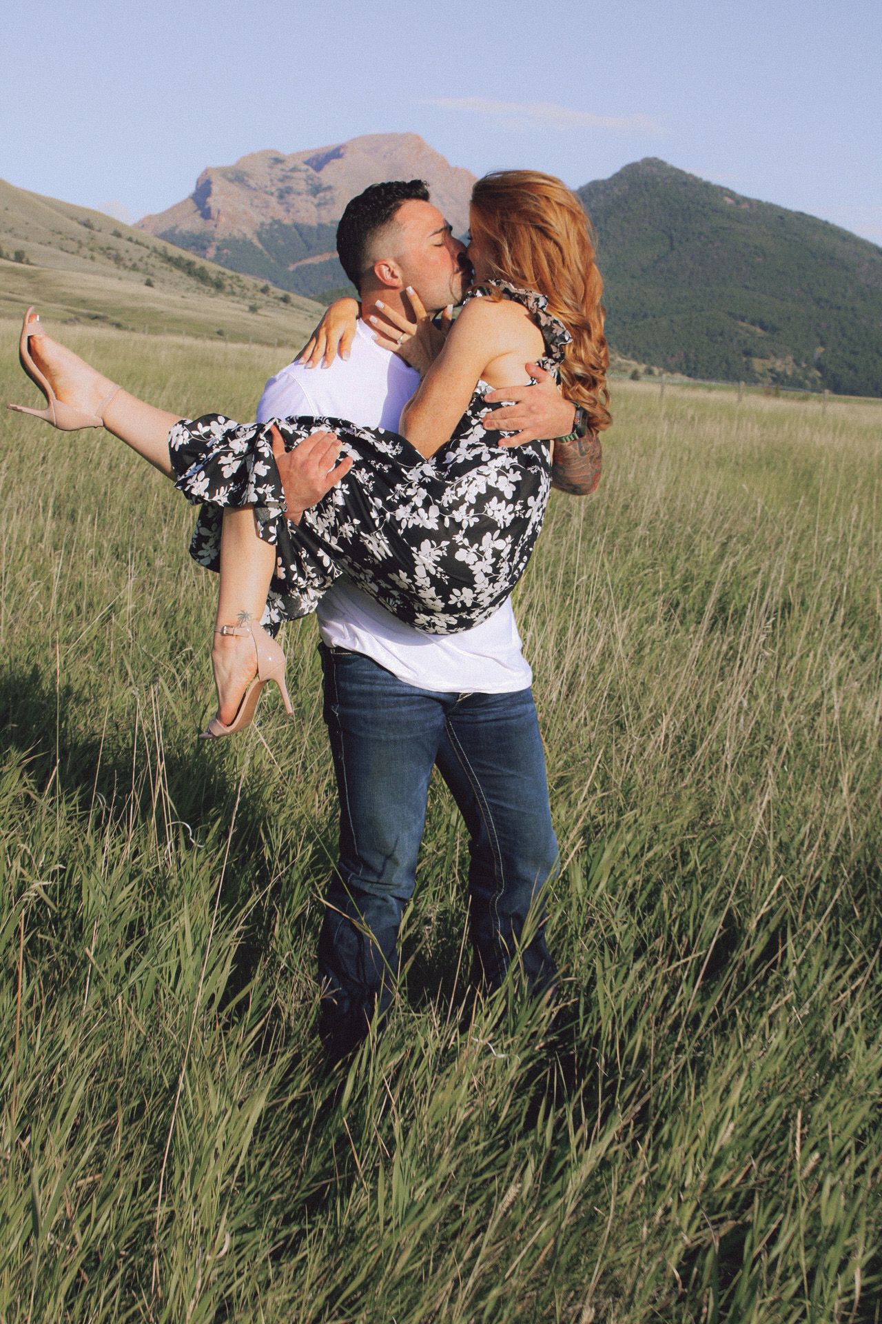 A romantic embrace in a Montana mountain meadow with tall grass and peaks in the distance at sunset.