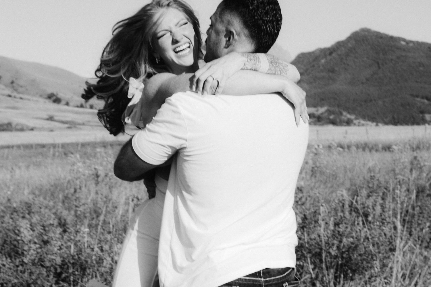 Romantic black and white photo series of a couple embracing and laughing together in a scenic outdoor field.