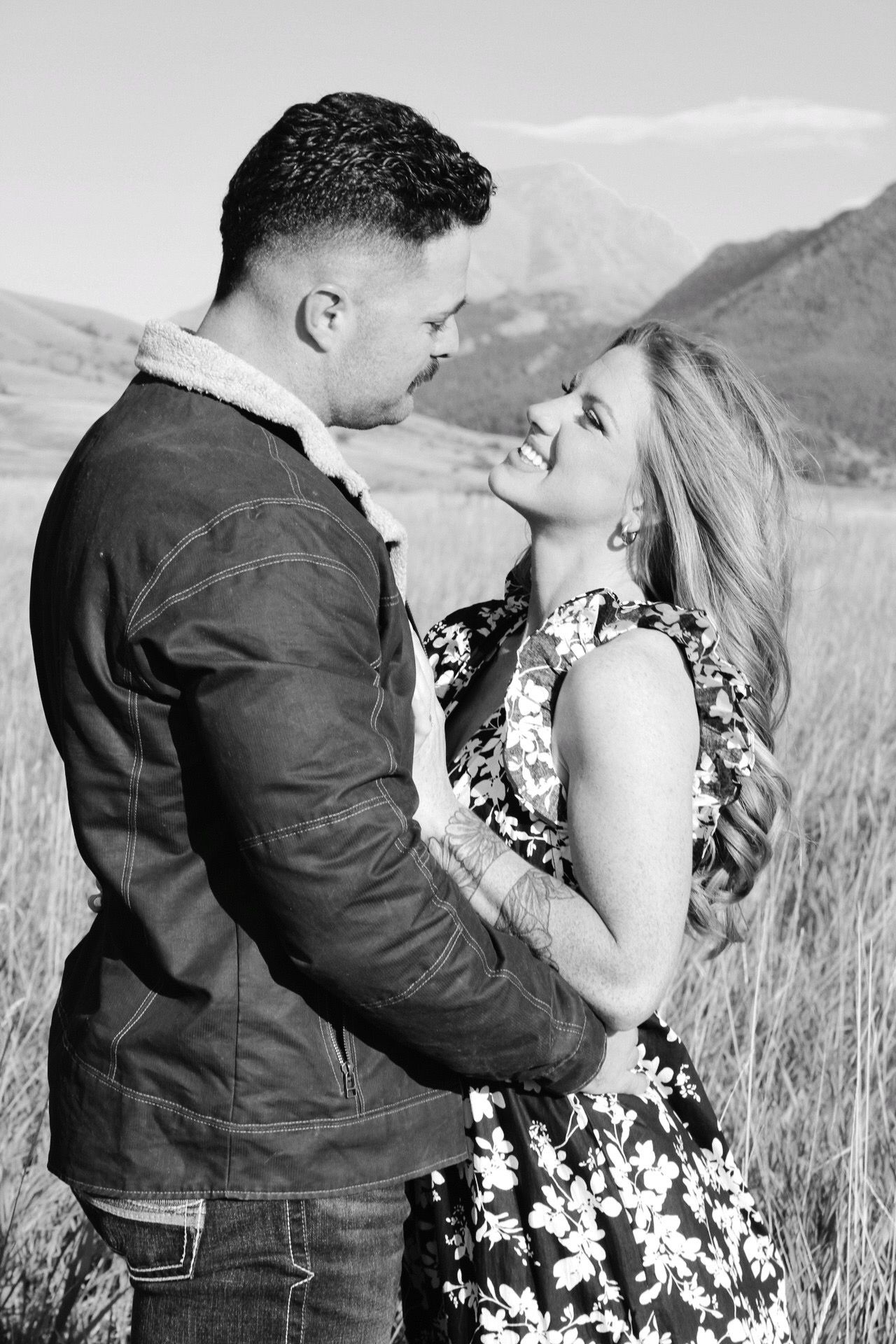 A romantic black and white photoshoot in a field shows a couple embracing against a Montana mountainous backdrop.