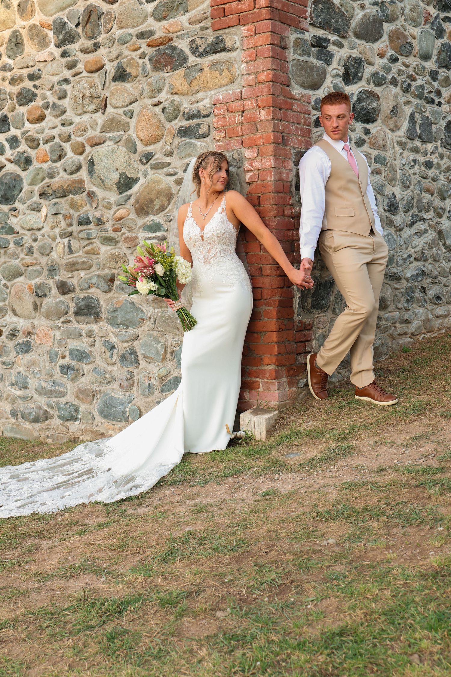 Wedding couple poses against rustic stone wall with brick accents in a series of artistic outdoor portraits.