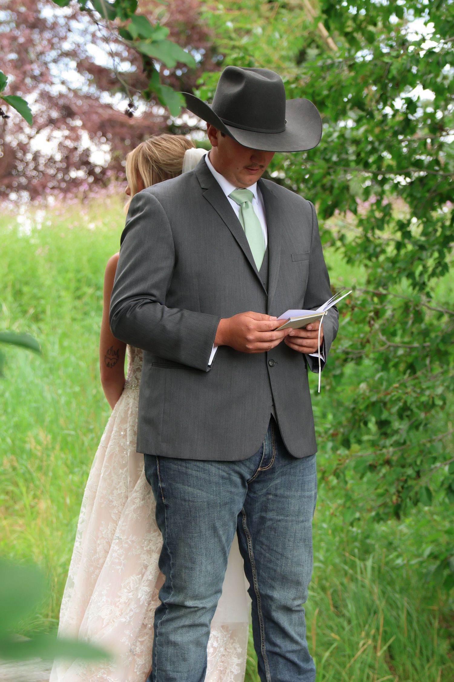 A groom in a cowboy hat and his bride read their private vows at an intimate Montana summer wedding.
