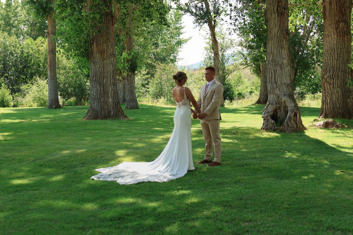 Five sequential photos show a couple sharing a romantic first look moment outdoors on a lush green lawn among tall trees.